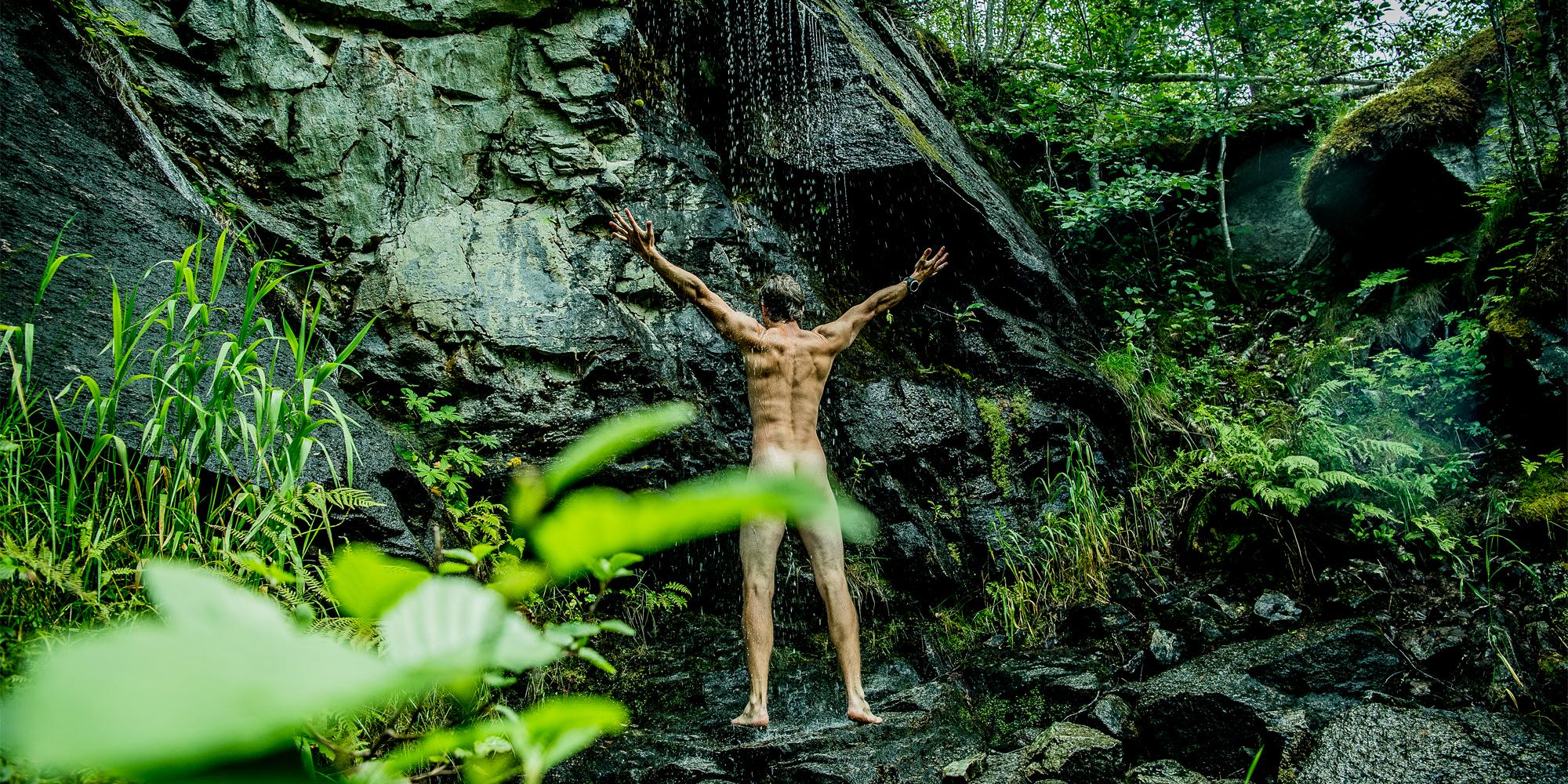 En mann som dusjer naken i en foss i Innerdalen
