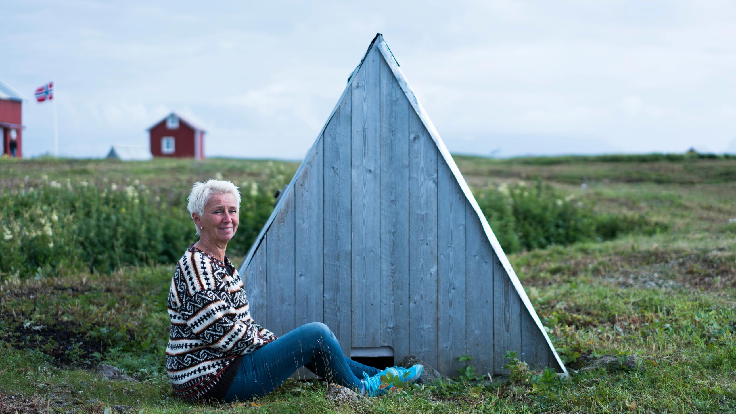 En kvinne sitter ved et ærfugl-hus på Lånan i Vega