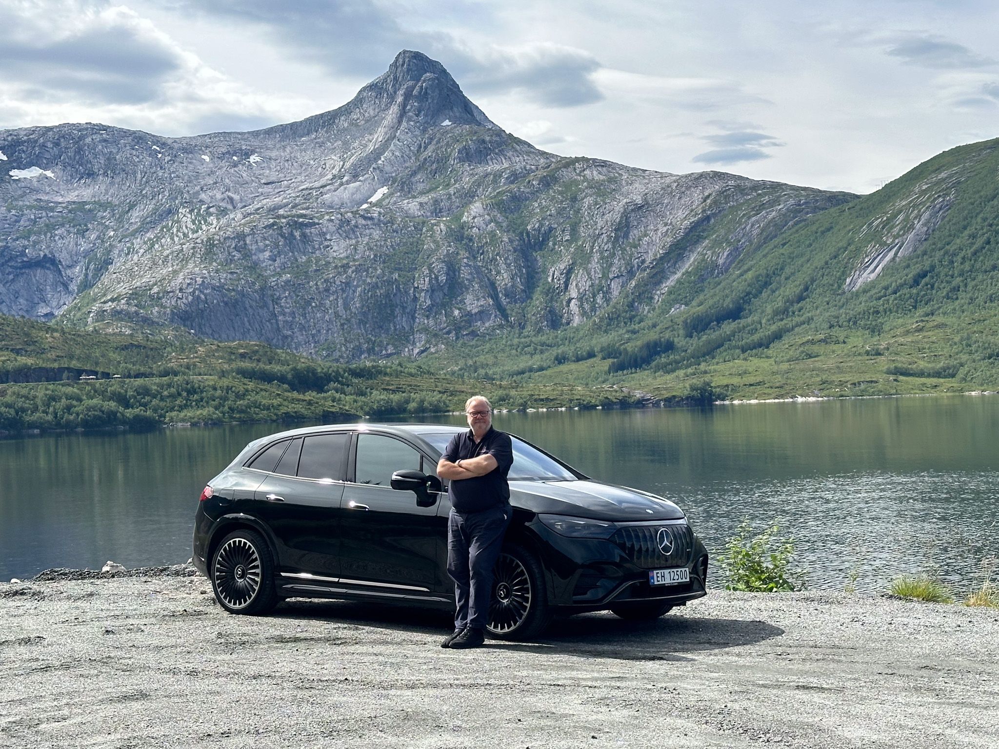 En man som står fremfor en elbil med flott norsk natur i bakgrunnen