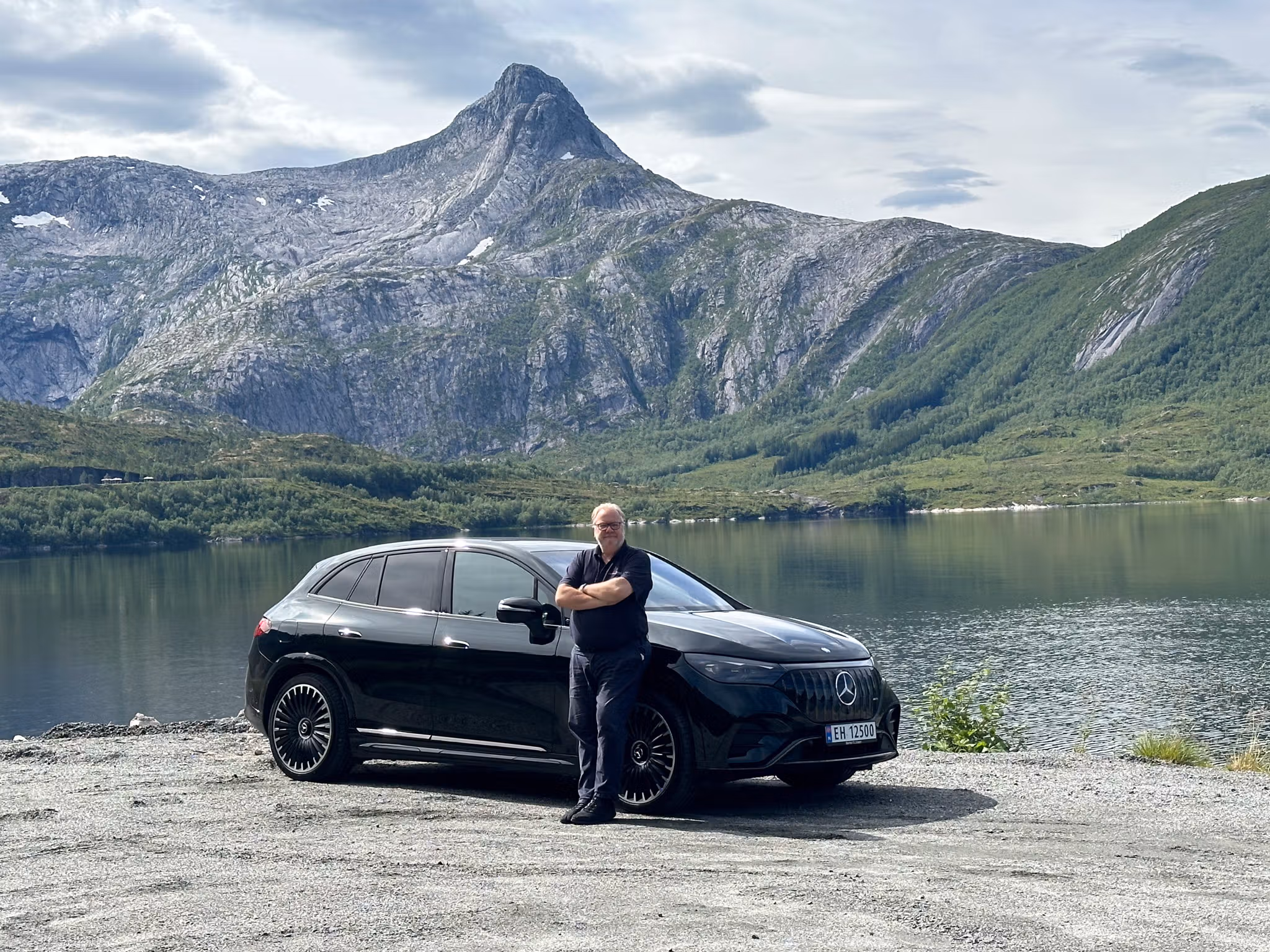 En man som står fremfor en elbil med flott norsk natur i bakgrunnen