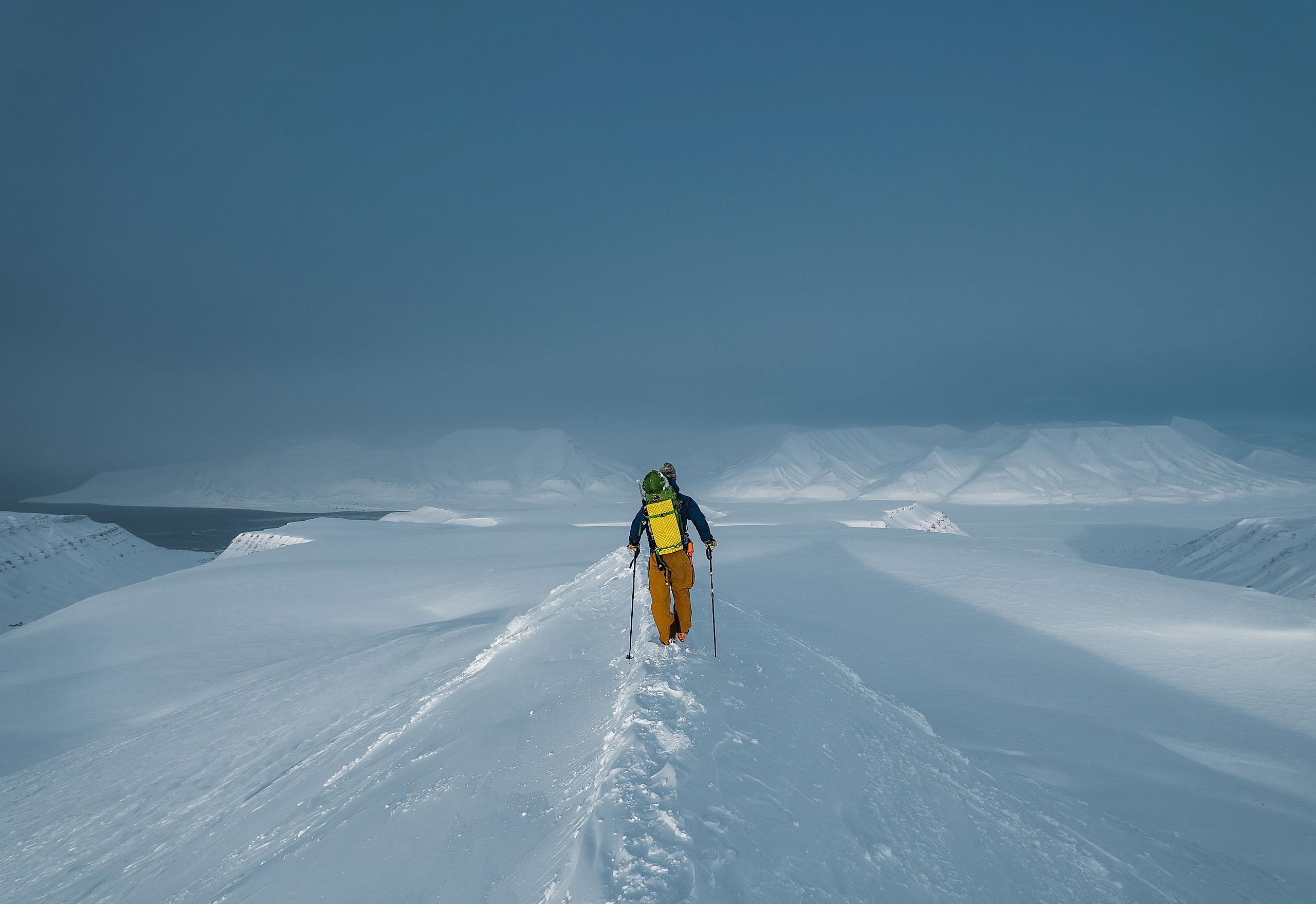 En person går mot de snødekte viddene på Svalbard