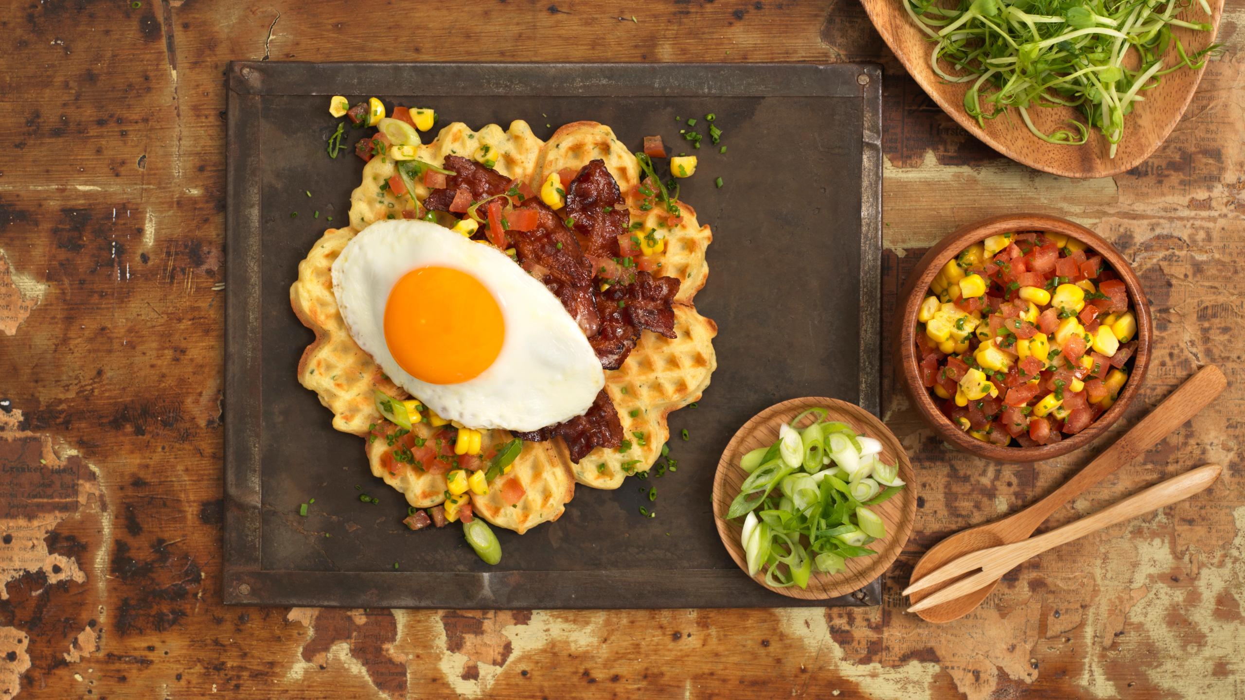 En tallerken med vaffel med egg, bacon og noen sideretter.