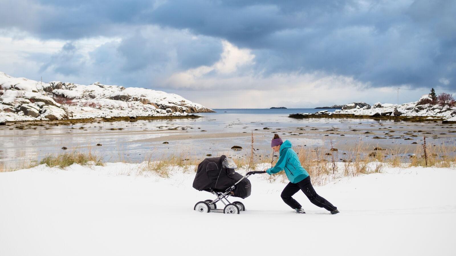 En dame dytter en barnevogn i snøen i Nord-Norge
