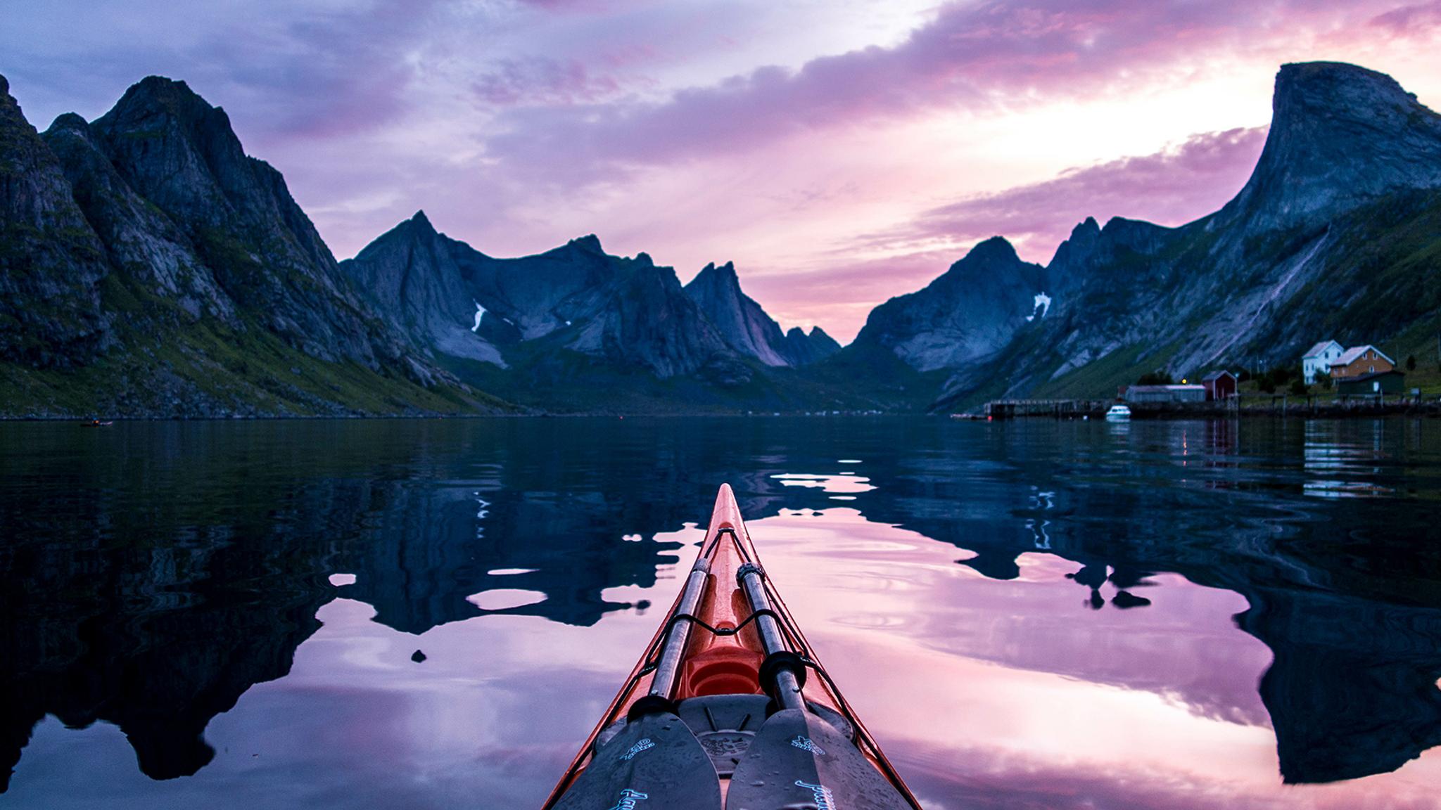 En kajak under midnattssolen i Moskenes i Lofoten, norra Norge, med höga bergstoppar i bakgrunden