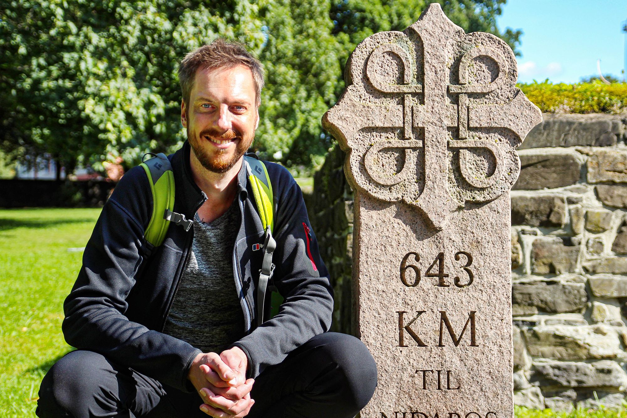 Pelgrim Kes Blans naast een bord dat de start aangeeft van de pelgrimsroute St-Olavsweg van Oslo naar Trondheim, Noorwegen.