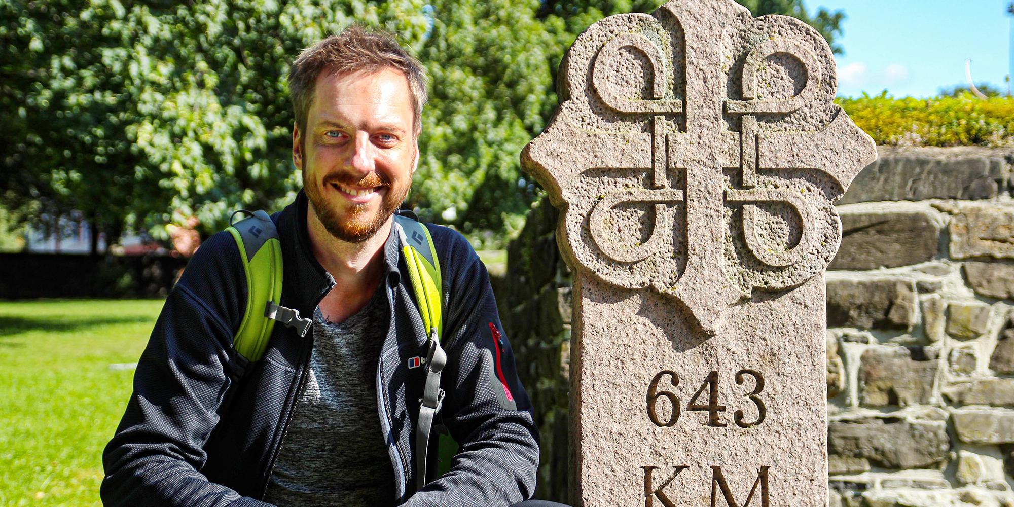 Pelgrim Kes Blans naast een bord dat de start aangeeft van de pelgrimsroute St-Olavsweg van Oslo naar Trondheim, Noorwegen.