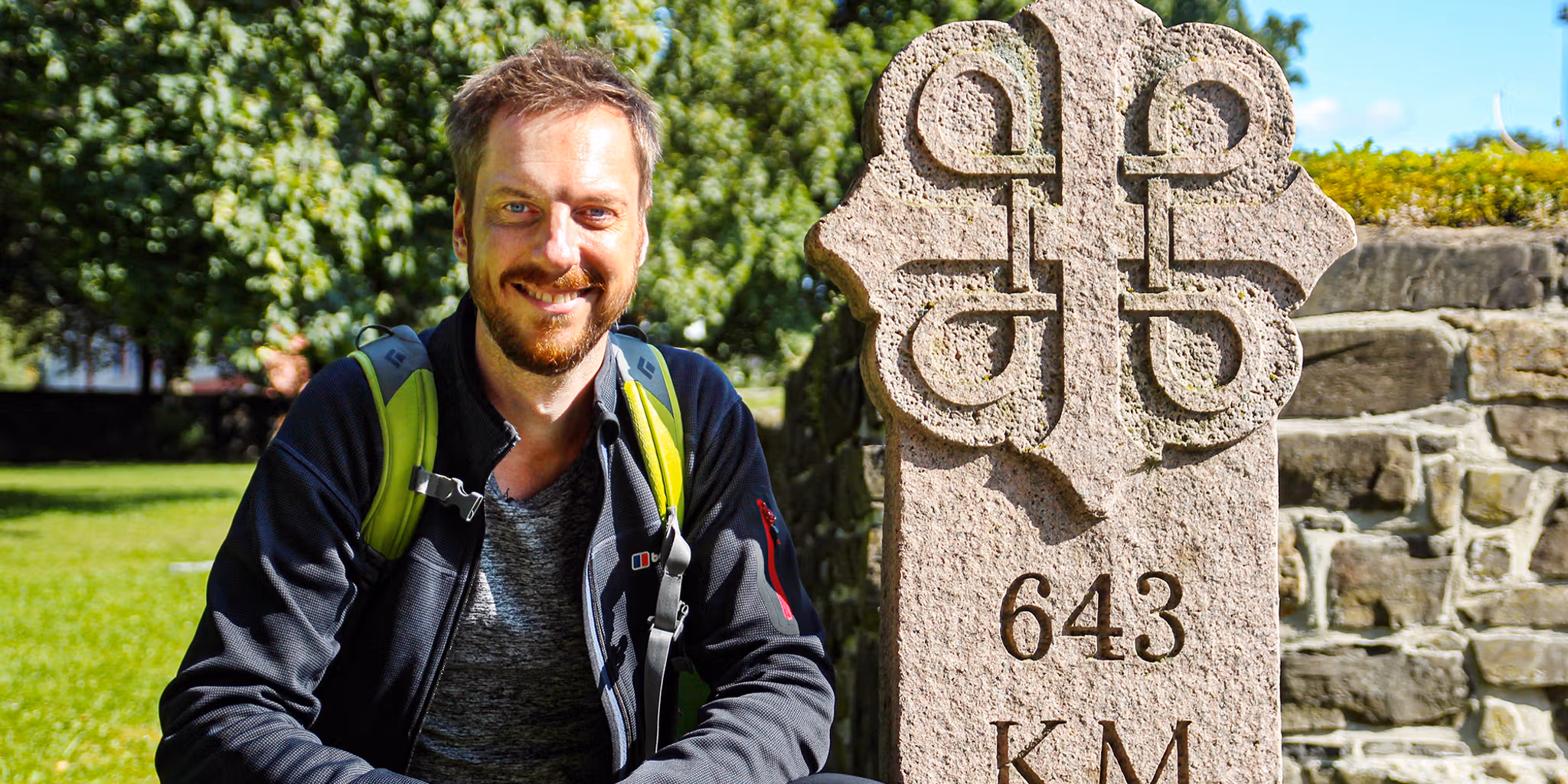 Pilgrimmen Kes Blans ved siden af et skilt, der markerer begyndelsen af Skt. Olavs-vejene fra Oslo til Trondheim, Norge