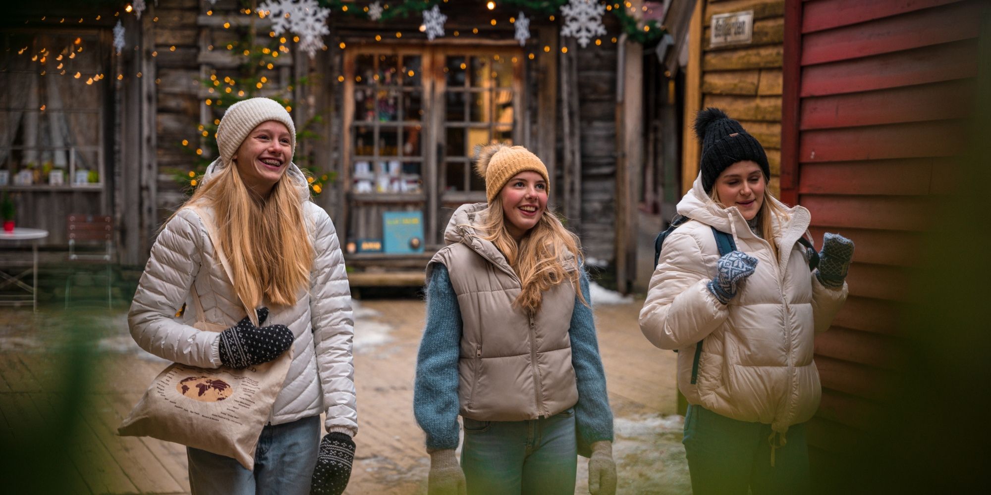 Tre jenter går mellom de juledepyntede trehusene på Bryggen i Bergen på Vestlandet