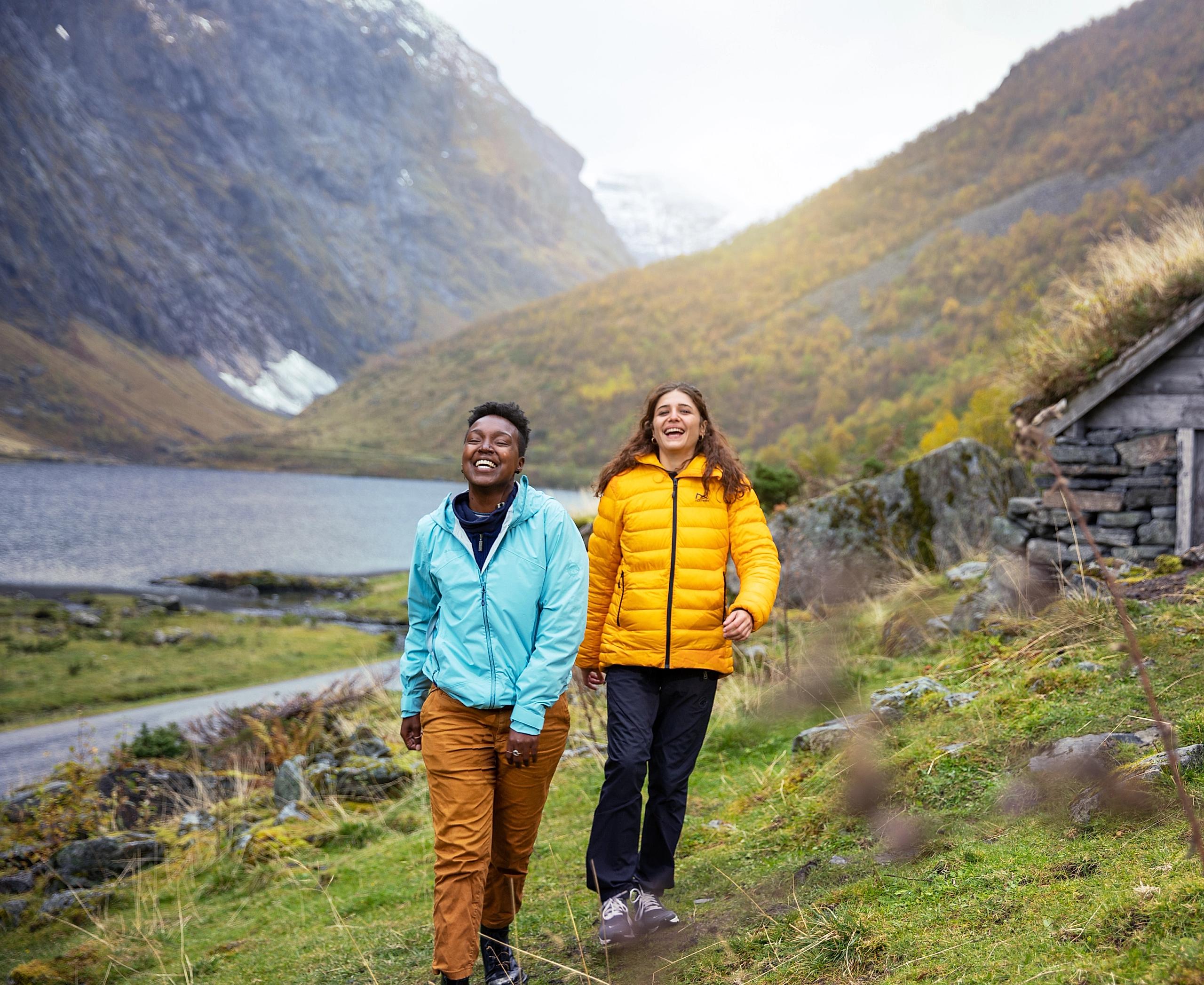 Dos mujeres hacen senderismo junto al fiordo Hjørundfjord, en la Noruega de los fiordos, en un día de otoño.