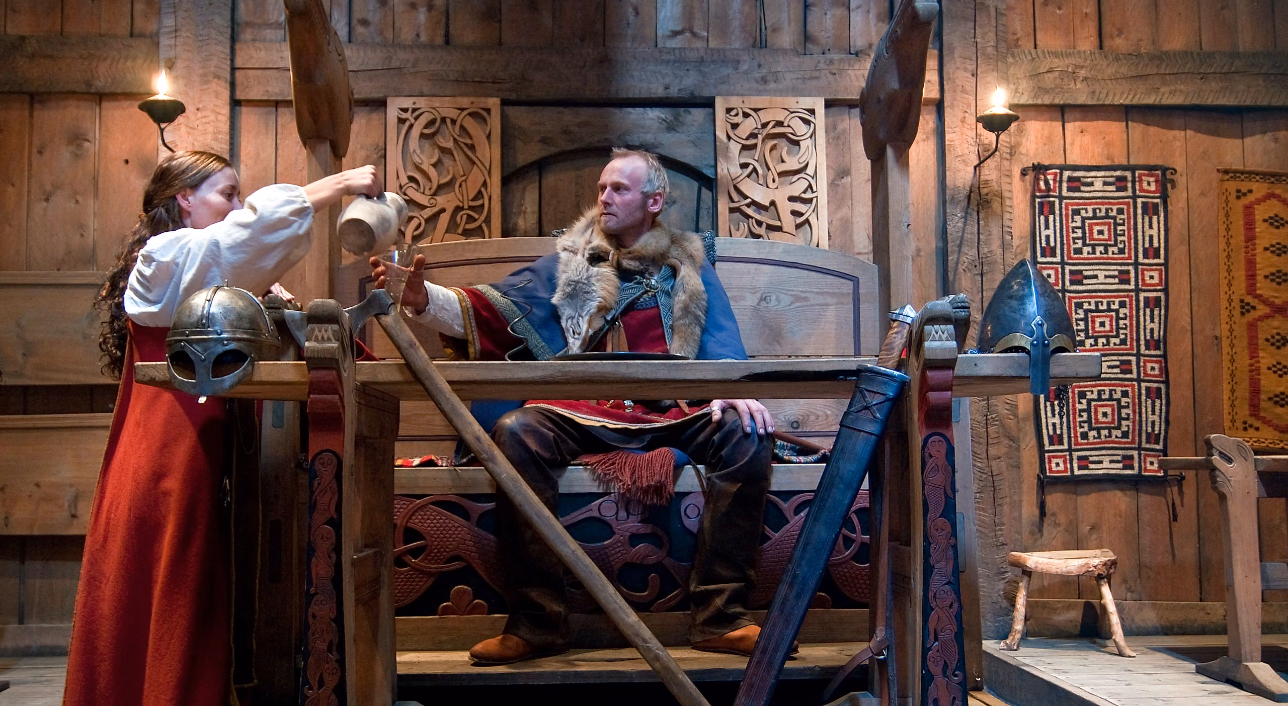 Viking throne with man and woman dressed as vikings in the Lofotr Viking Museum in Lofoten, Northern Norway