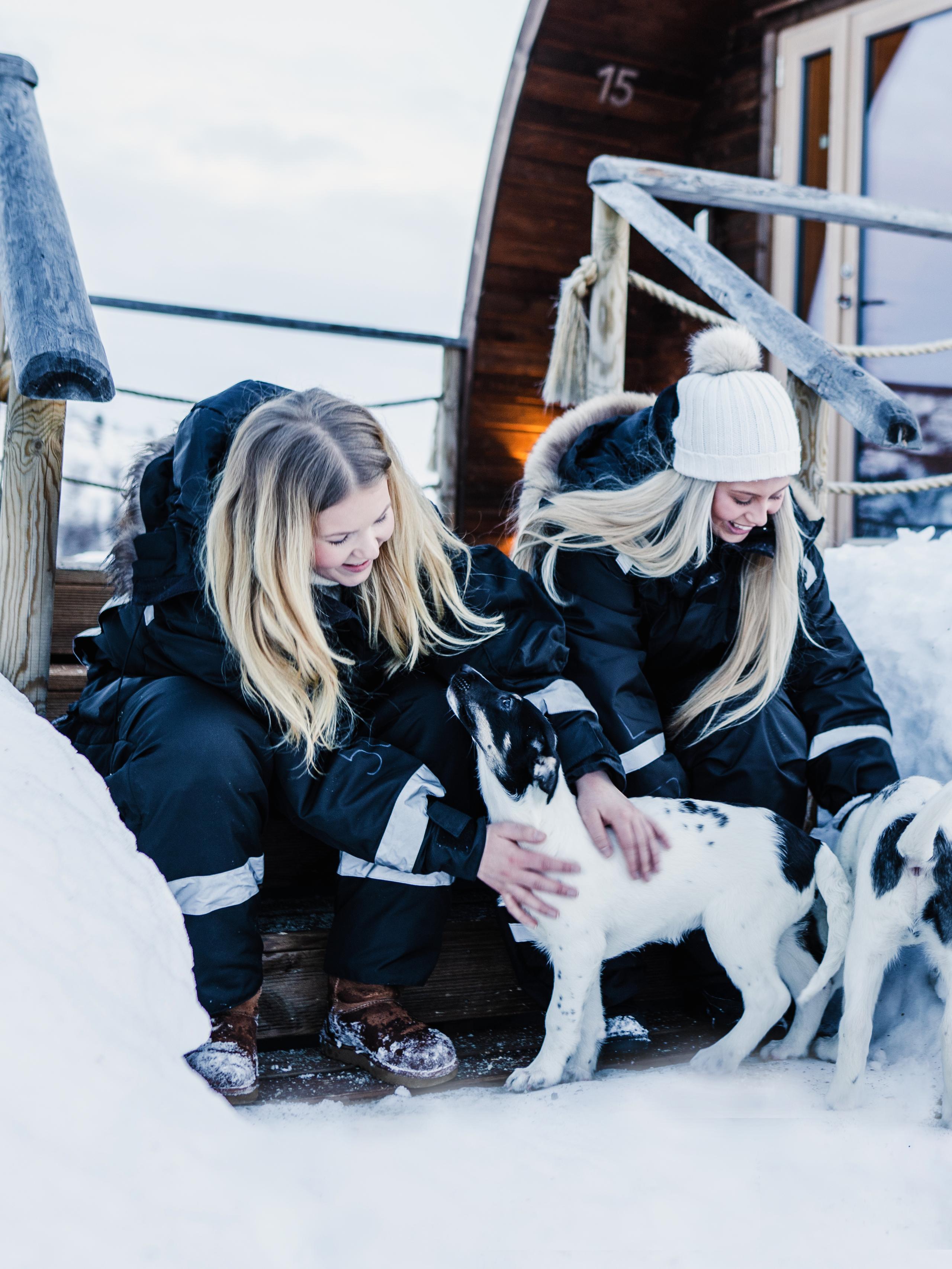 To jenter klapper huskyvalper utenfor Snowhotel Kirkenes
