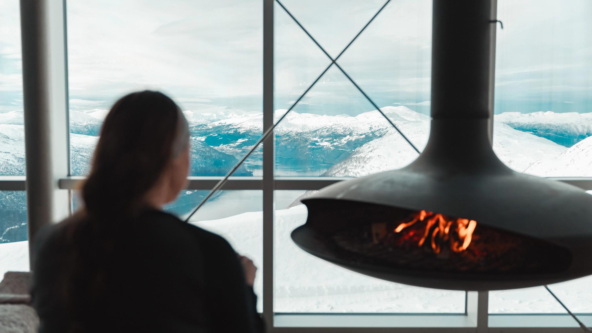 A woman by a fireplace with a hot chocolate.