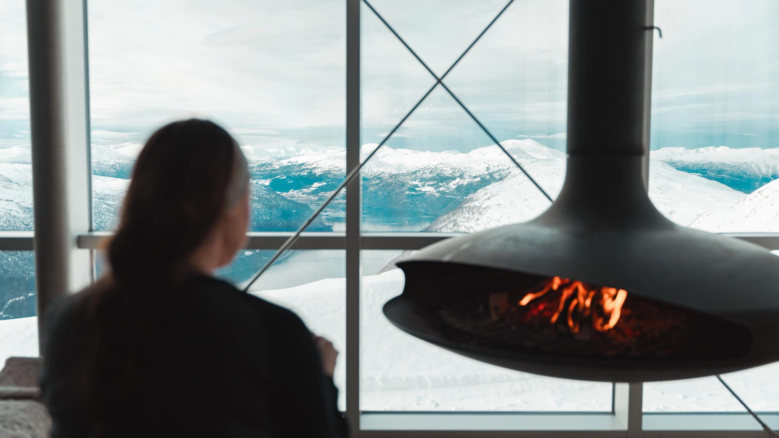 A woman by a fireplace with a hot chocolate.