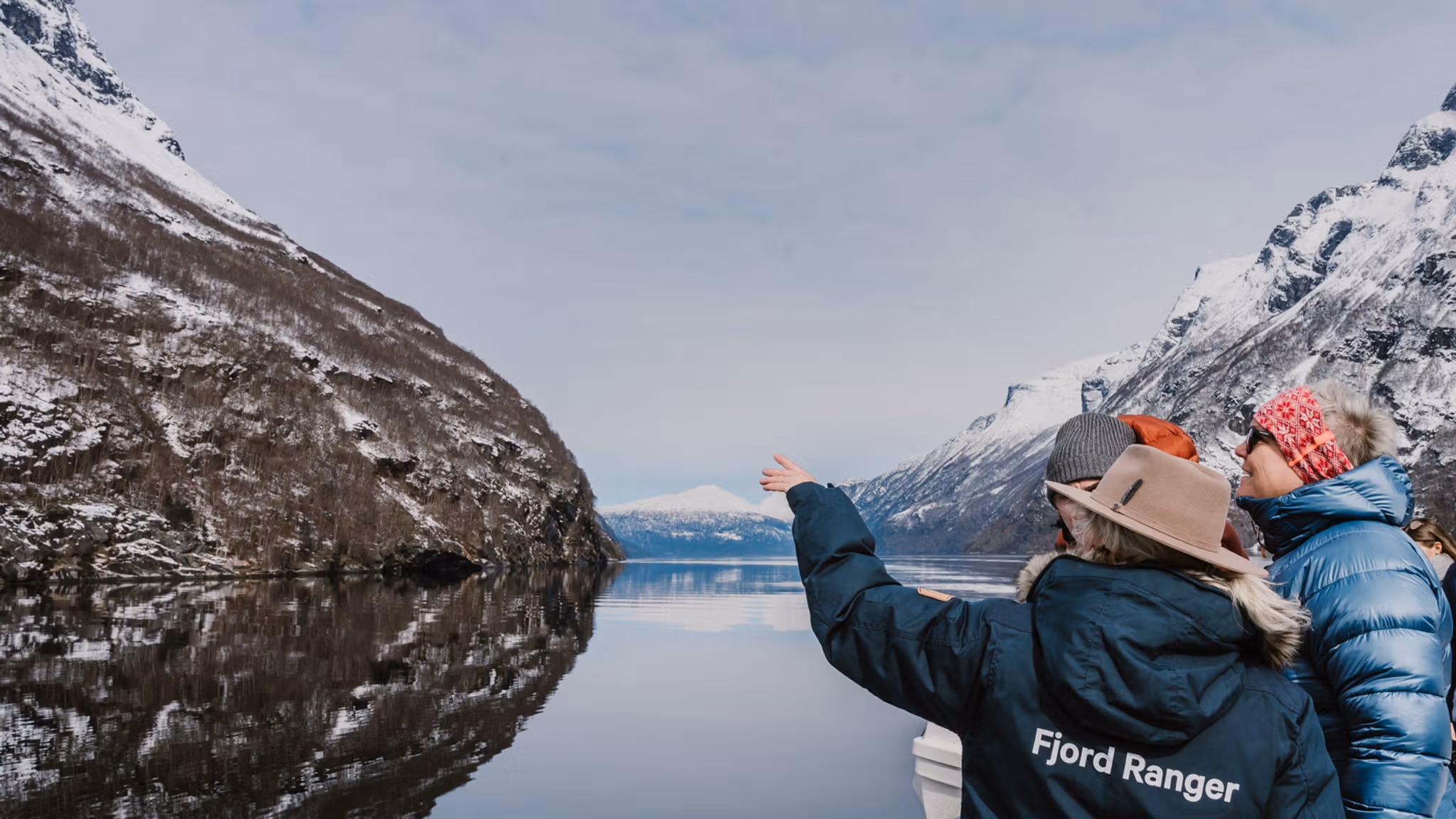 Three people pointing at a mountain while on a wintercruise in Geirangerfjorden, Sunnmøre.