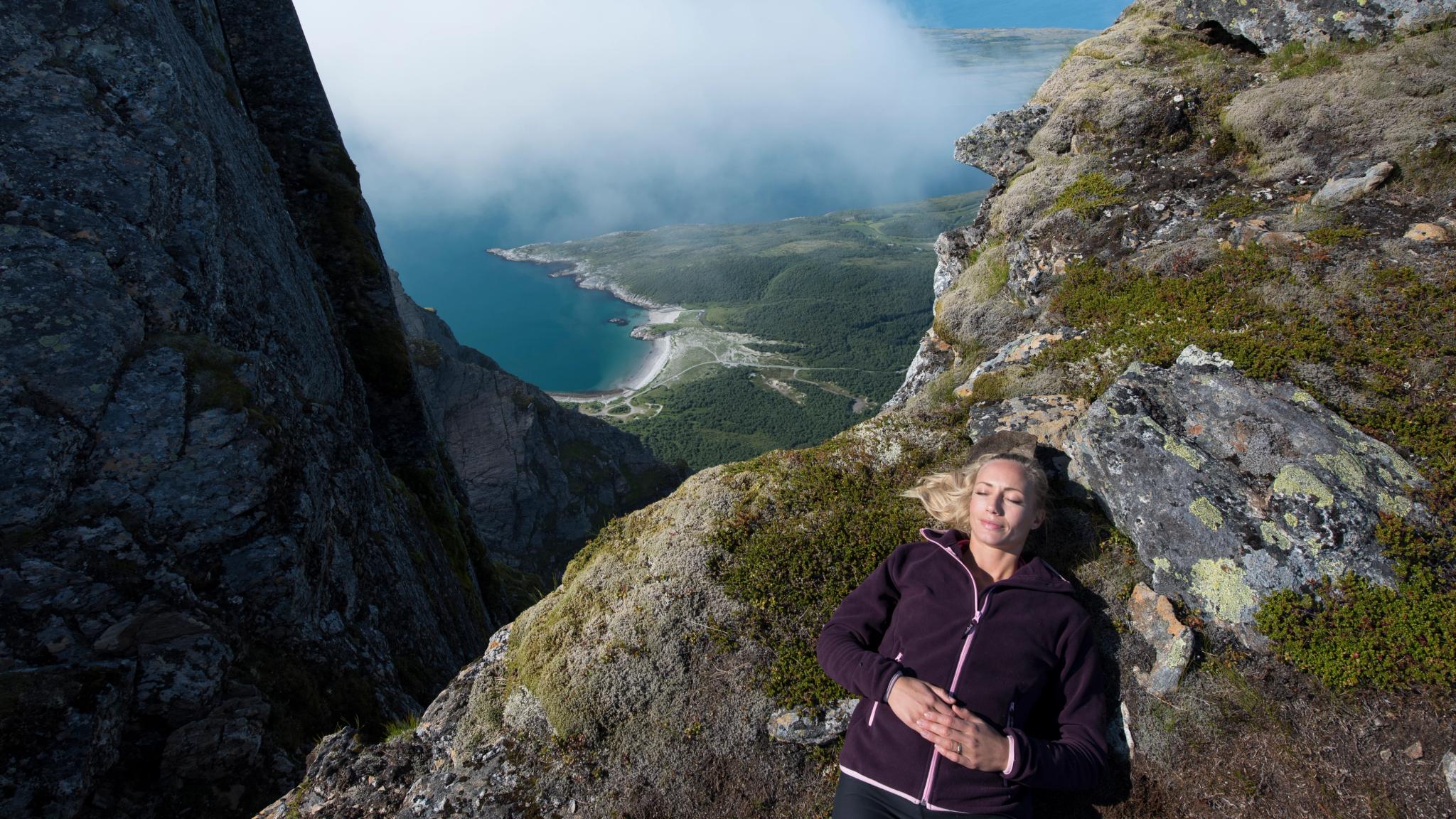 Una mujer se toma un descanso durante una jornada de senderismo por la montañas de Dønnamannen, en Helgeland, Norte de Noruega, con el océano de fondo.
