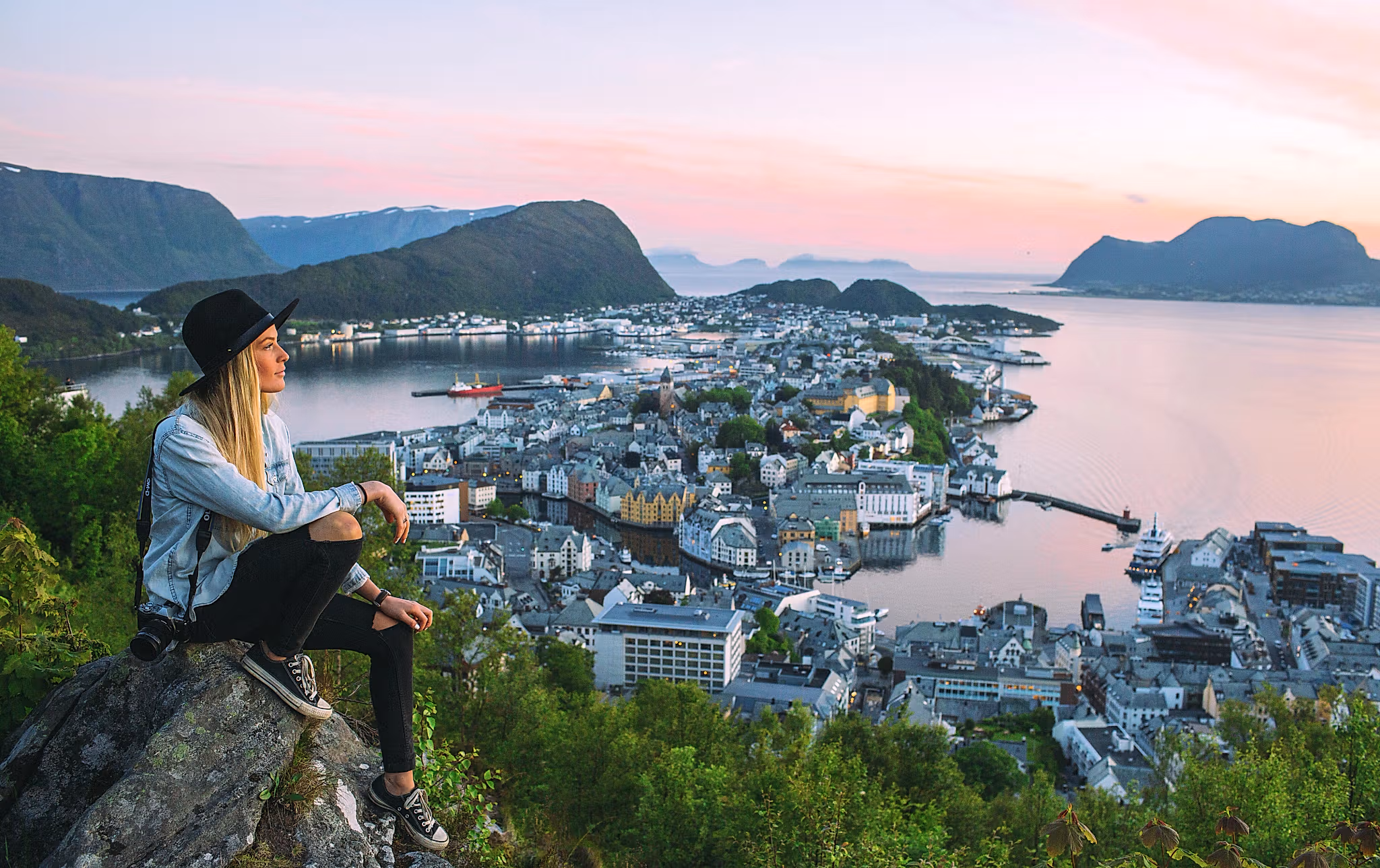 Woman sitting at the top of Aksla mountain in Ålesund city with a pink sunset, Fjord Norway