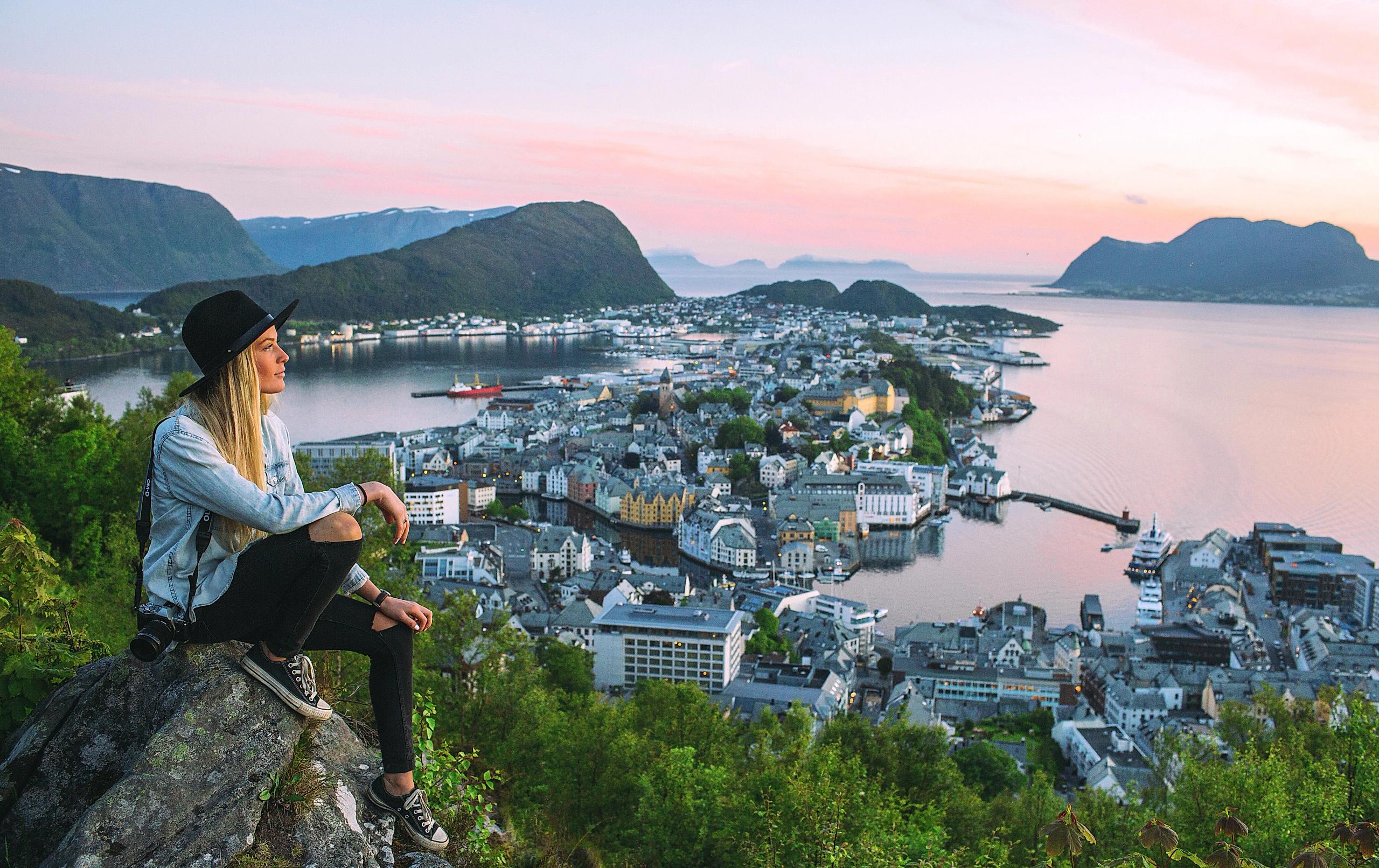 Woman sitting at the top of Aksla mountain in Ålesund city with a pink sunset, Fjord Norway