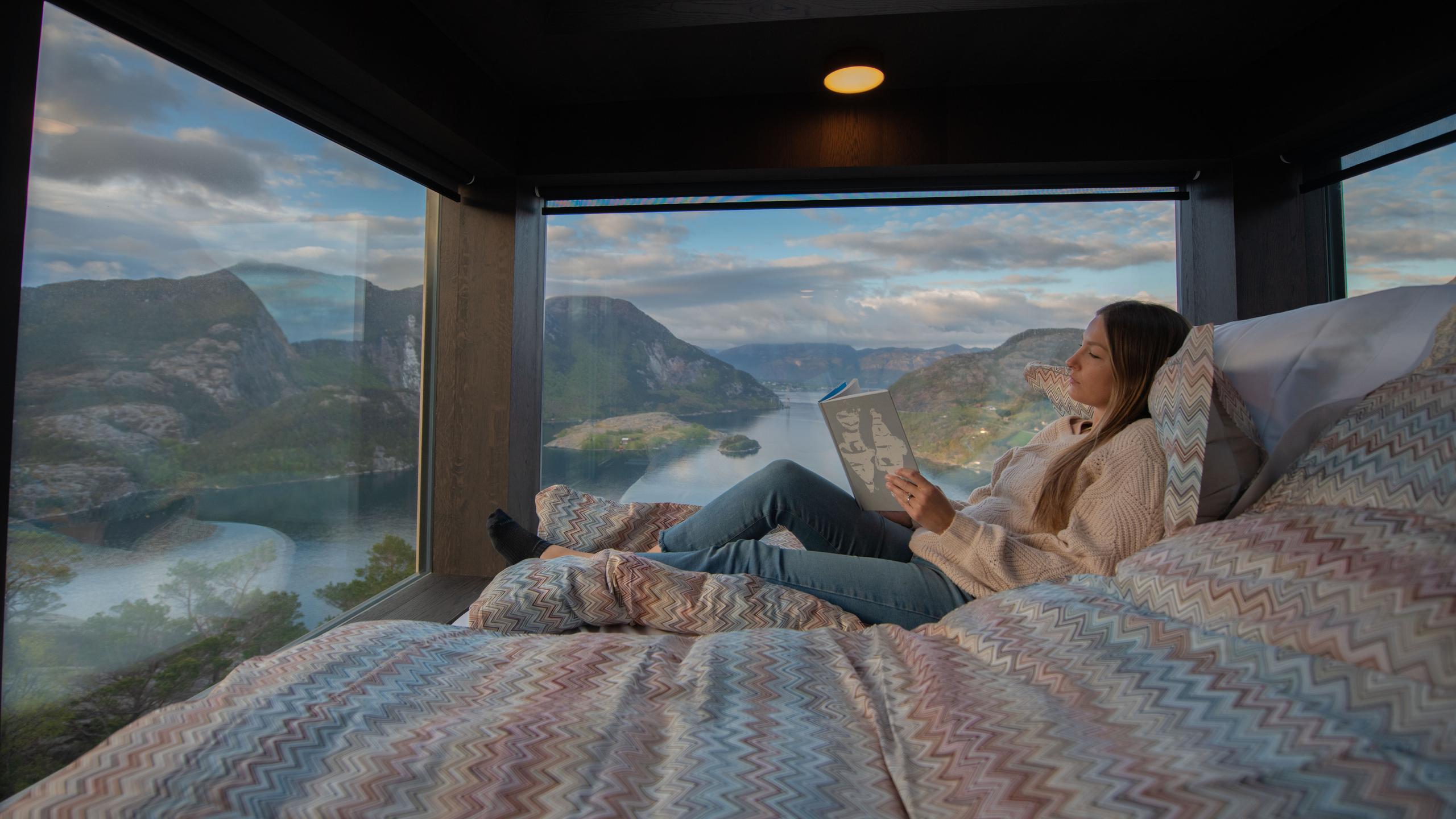 En dame leser på sengen på The Bolder Sky Lodges ved Lysefjorden i Ryfylke, Vestlandet