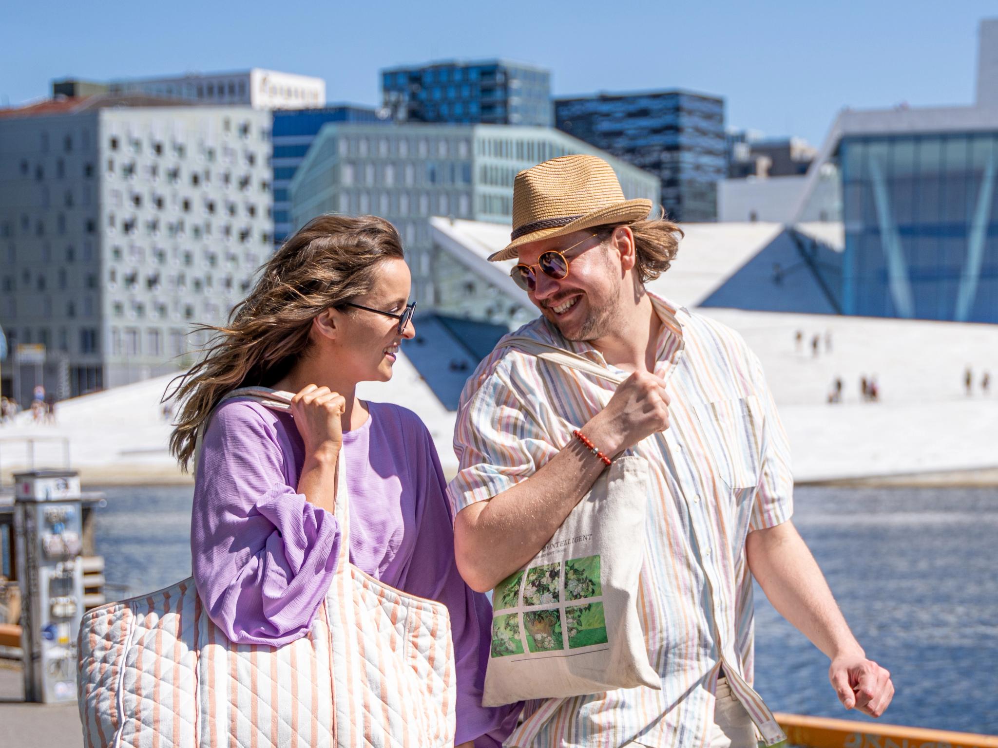 Man and woman walking the Oslo harbour promenade, the Opera house in the back