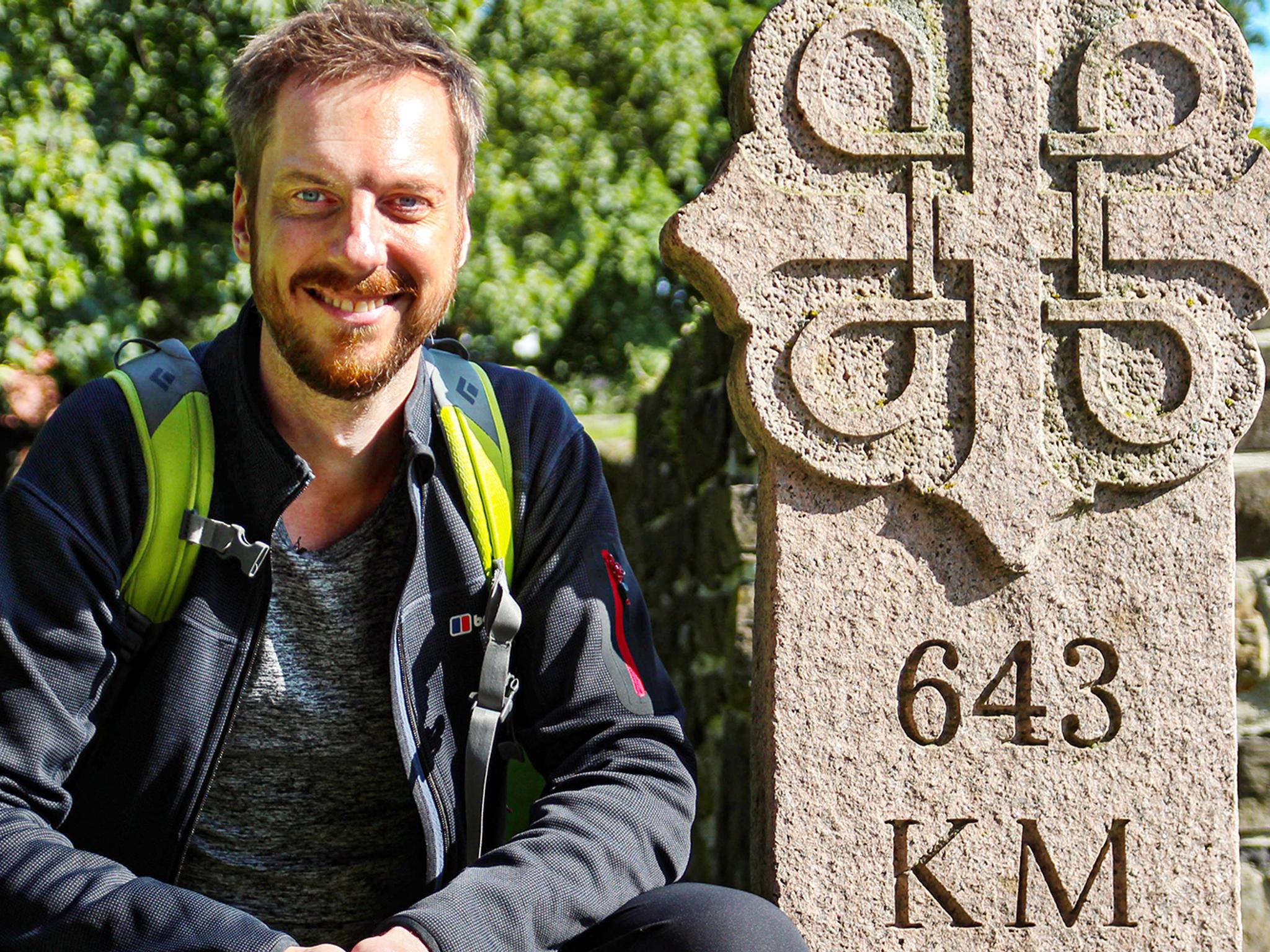 Pilgrim Kes Blans next to a sign that marks the start of the St. Olav Ways pilgrim path from Oslo to Trondheim, Norway