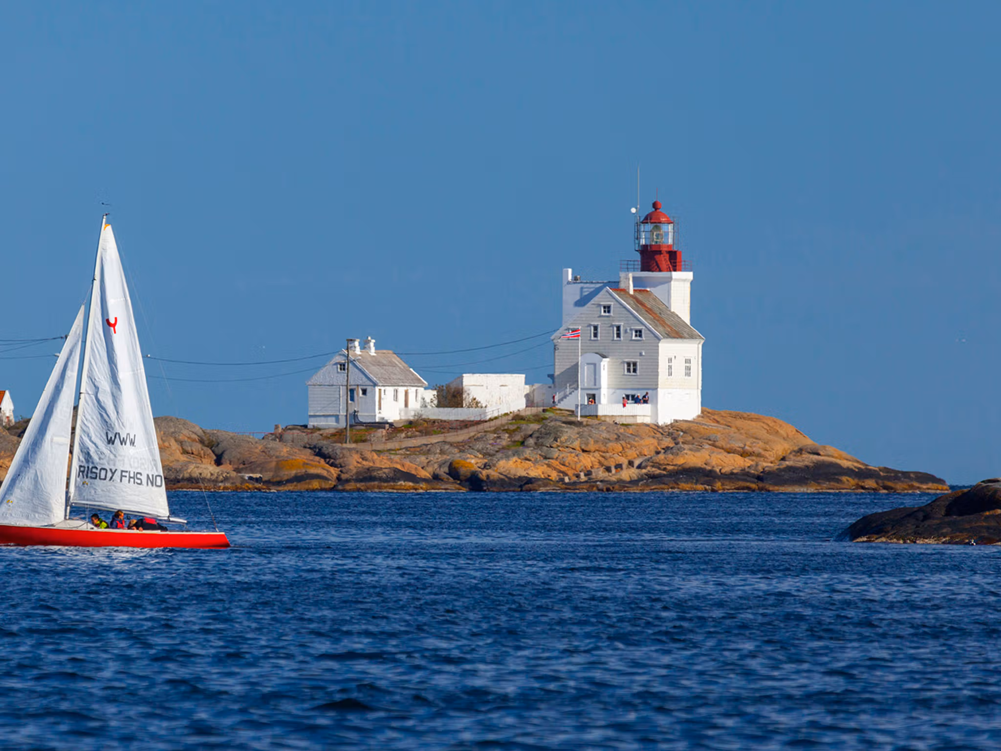 A sailboat passing by the Lyngør lighthouse during summer in Southern Norway.