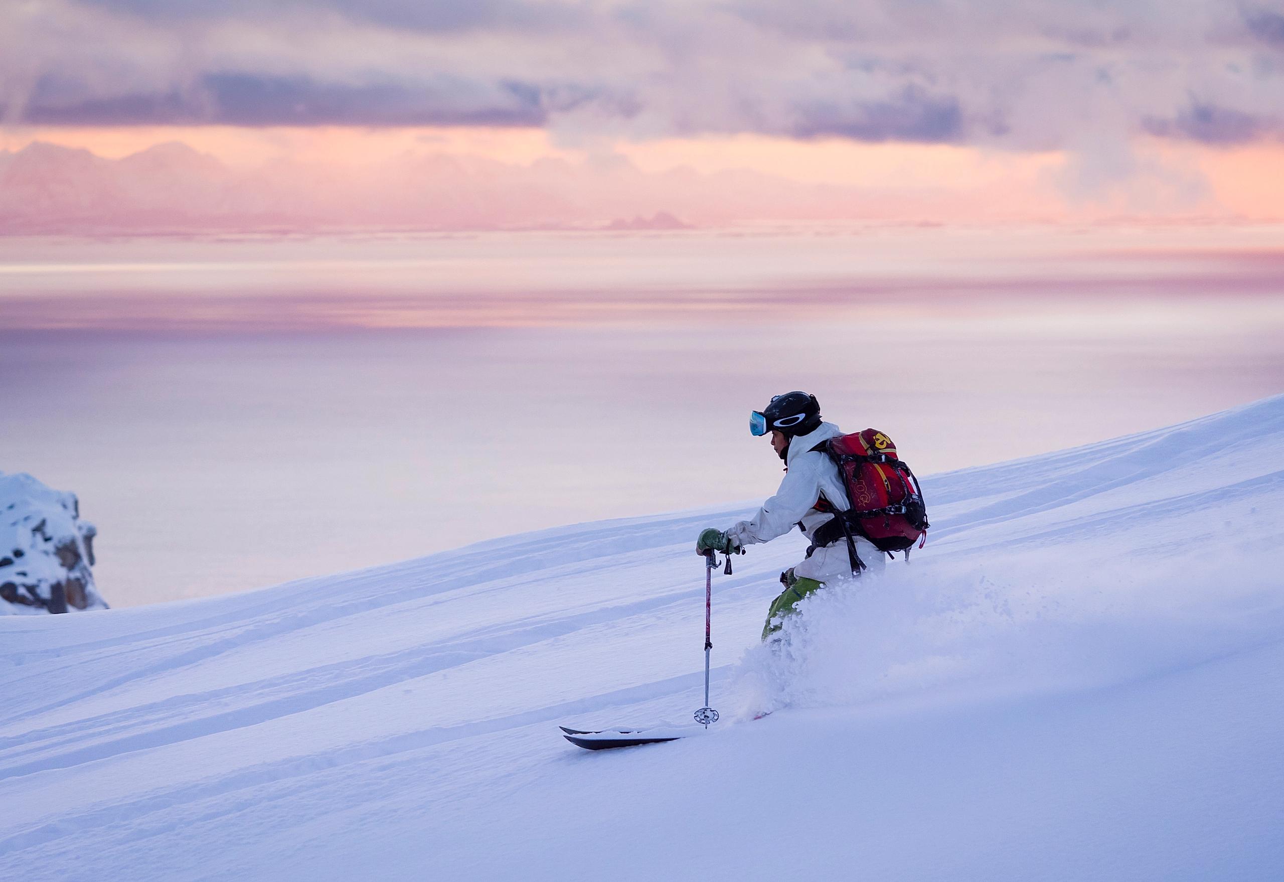 Kvinne står på ski ned fjellsiden på Småtindan under en rosa himmel i Lofoten