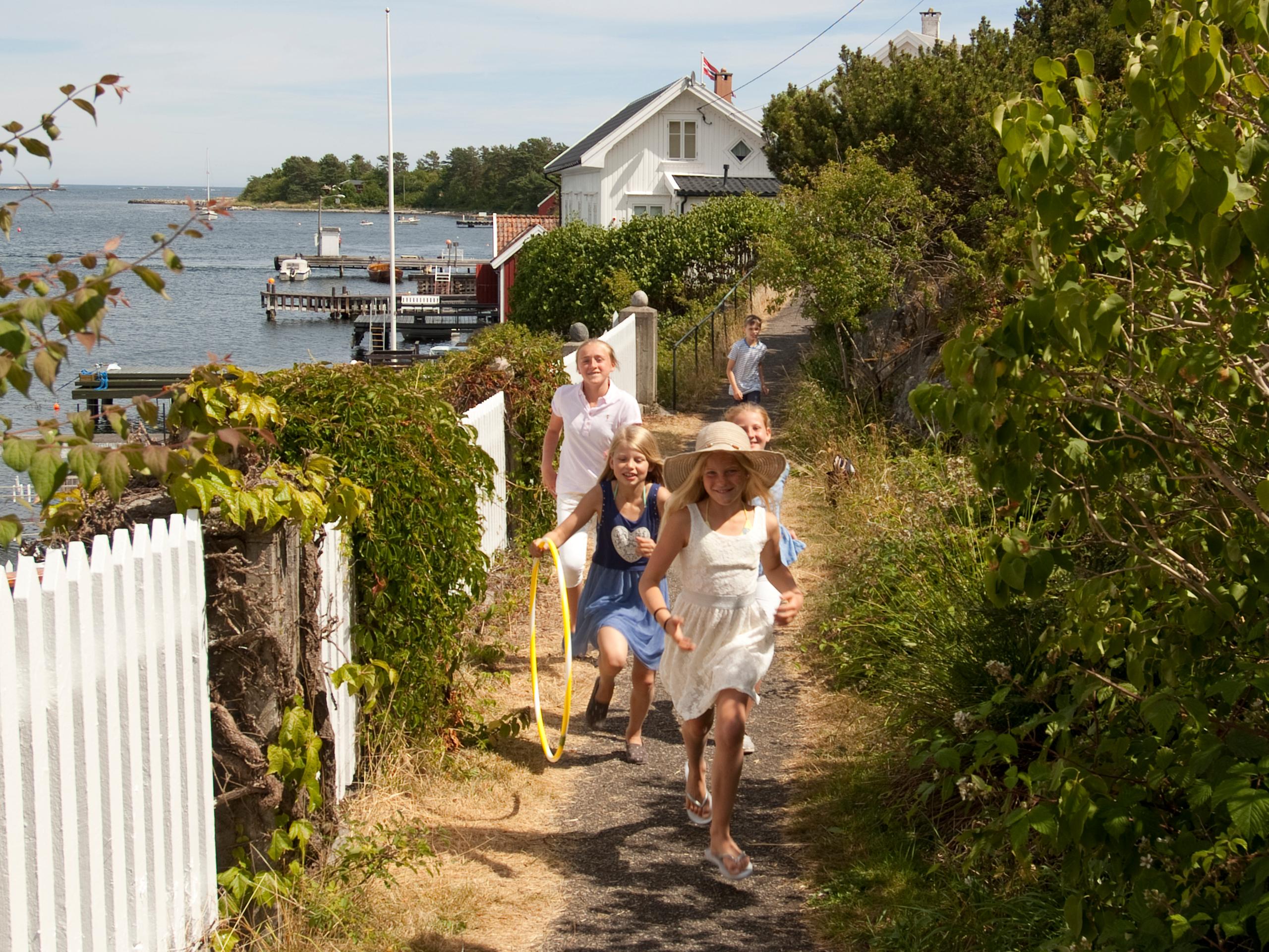 A group of children running along a white picket fence on Merdø island in Arendal, Southern Norway.