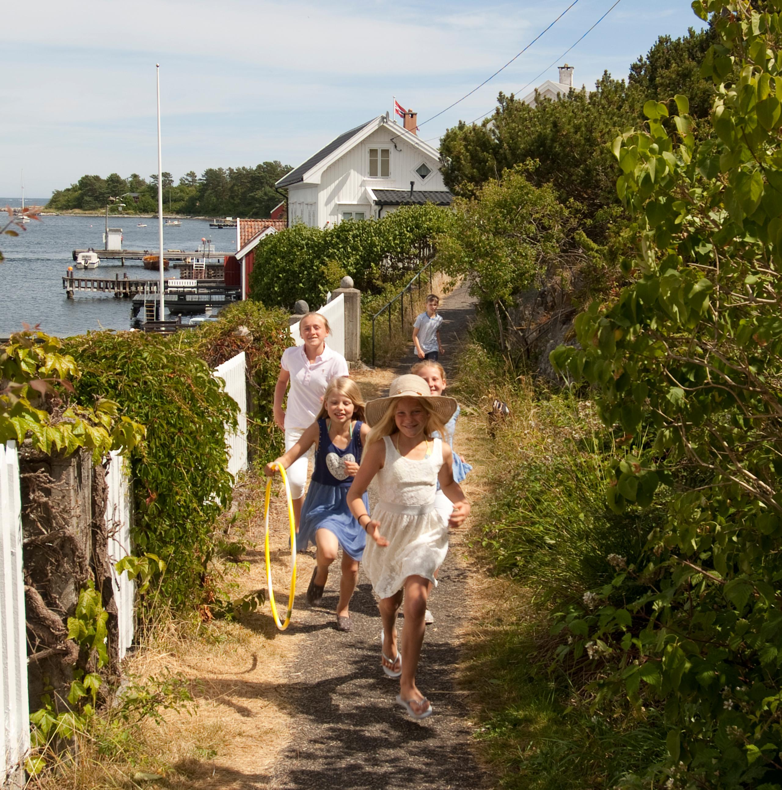 A group of children running along a white picket fence on Merdø island in Arendal, Southern Norway.