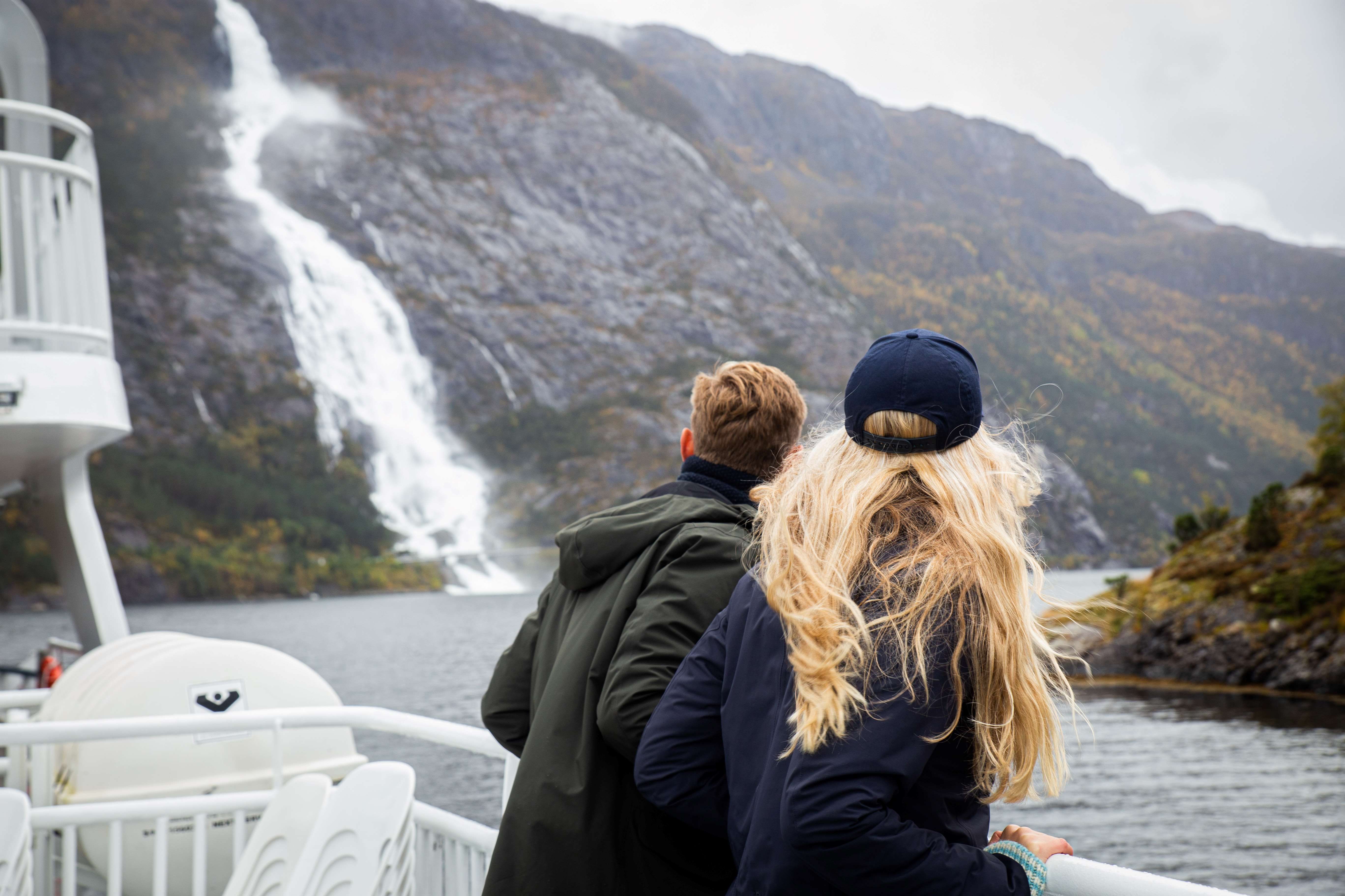 A couple at a fjord cruise looking at a waterfall.