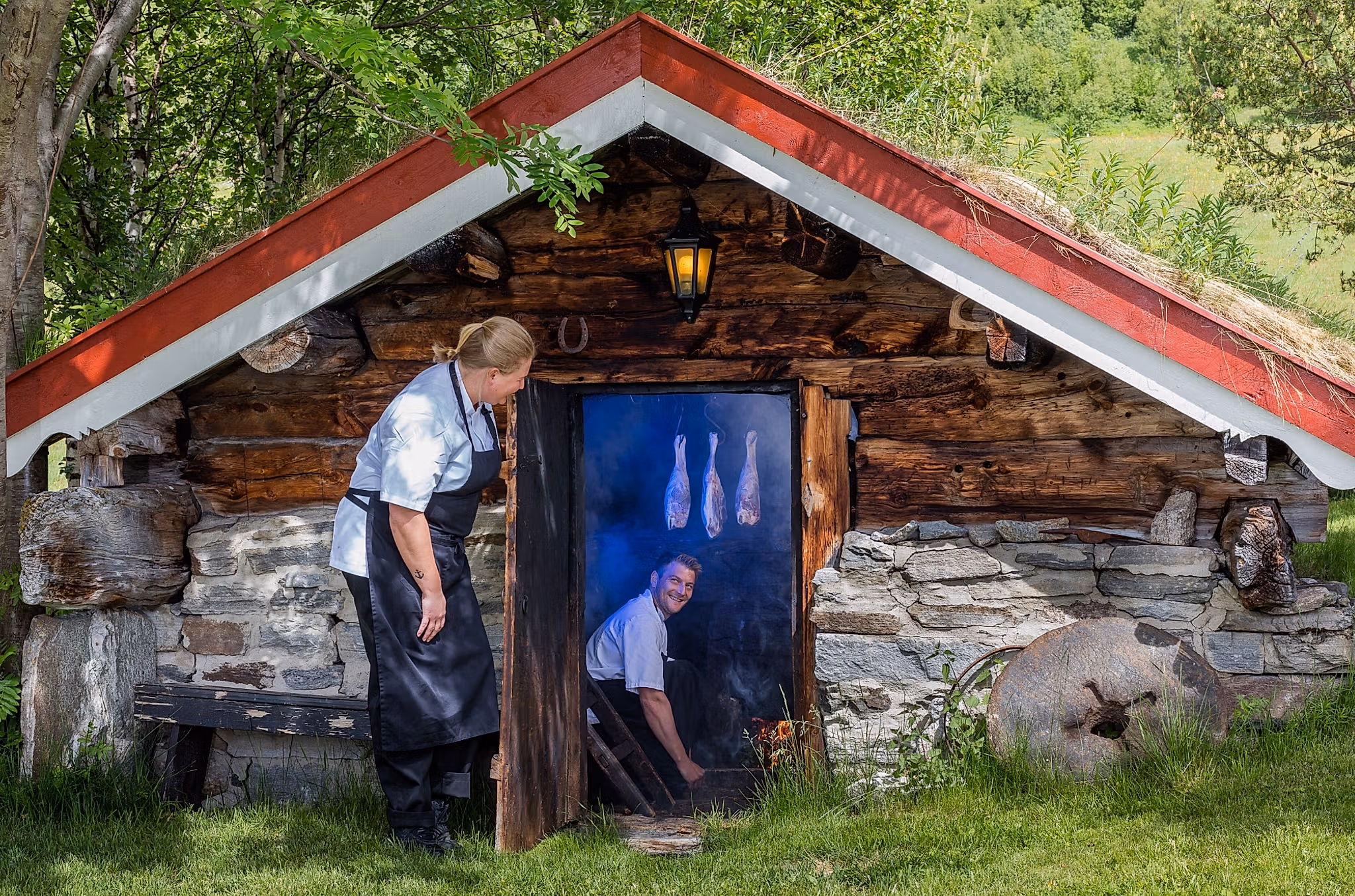 En mann lager røkt lammelår i en røykbadstu på Bortistu gjestegard i Oppdal i Trøndelag