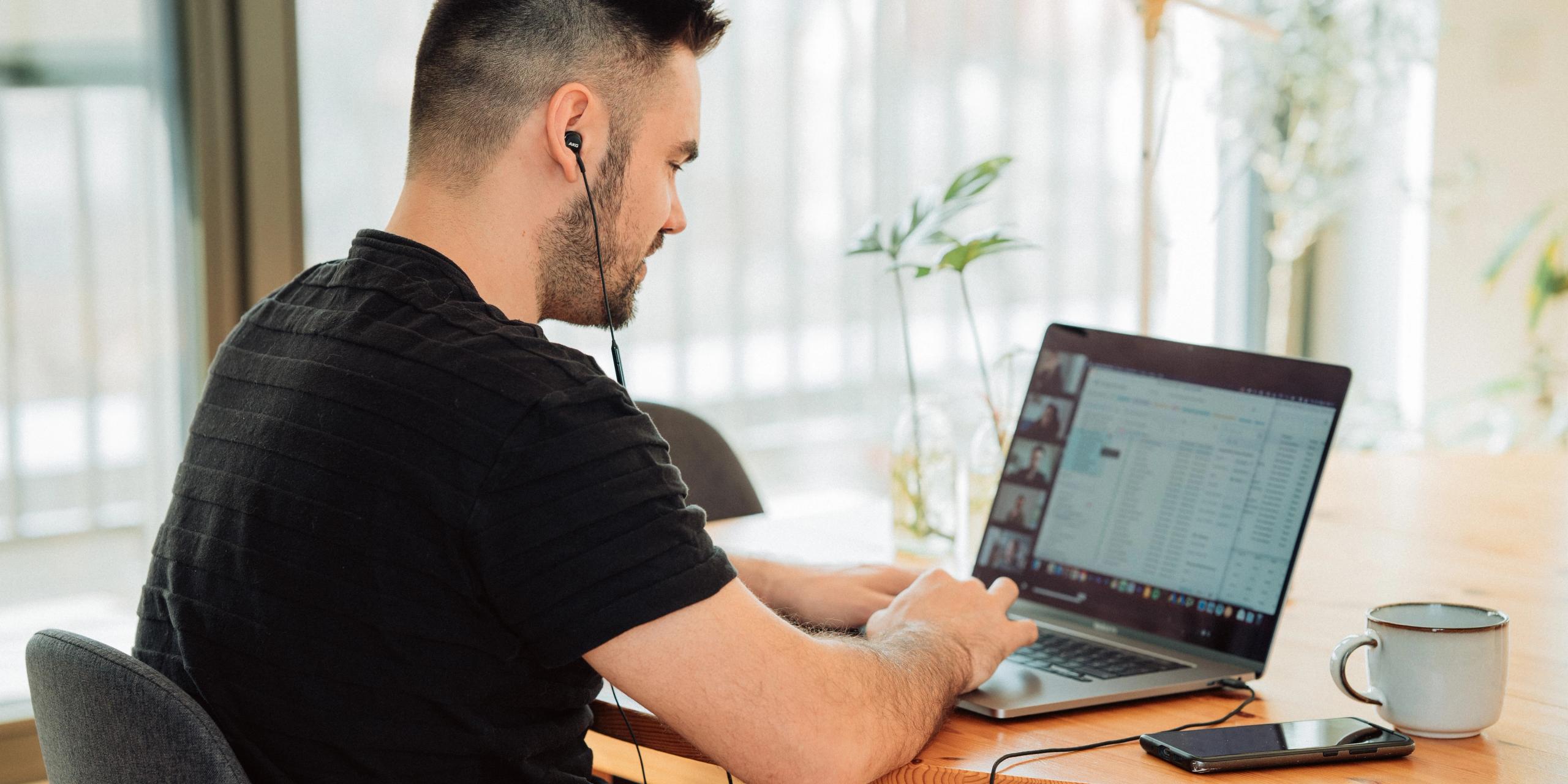 A young man in a black T-shirt in a conference meeting on his laptop