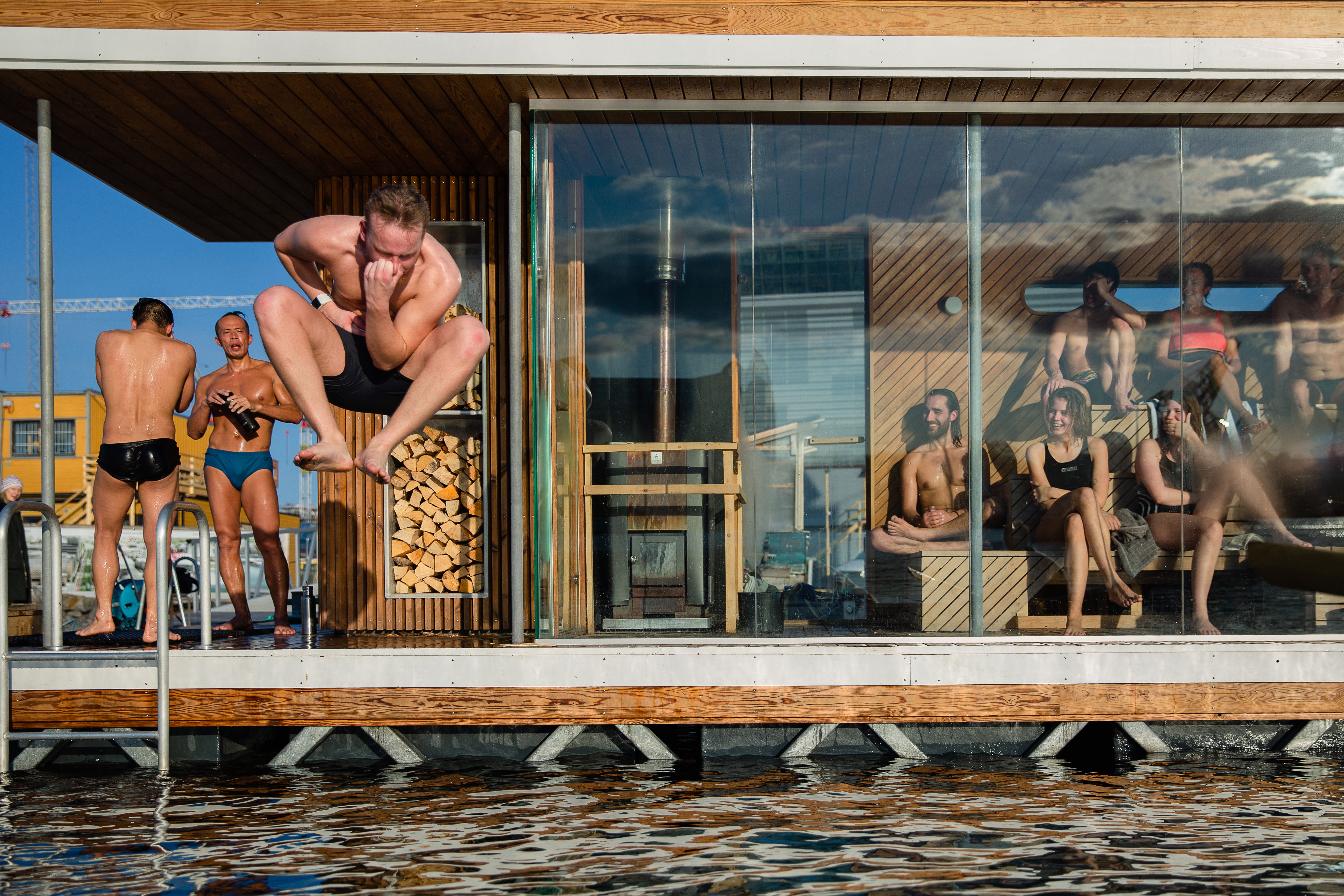 People enjoying a sauna session at Oslo Fjord Sauna. One man is jumping in the sea.