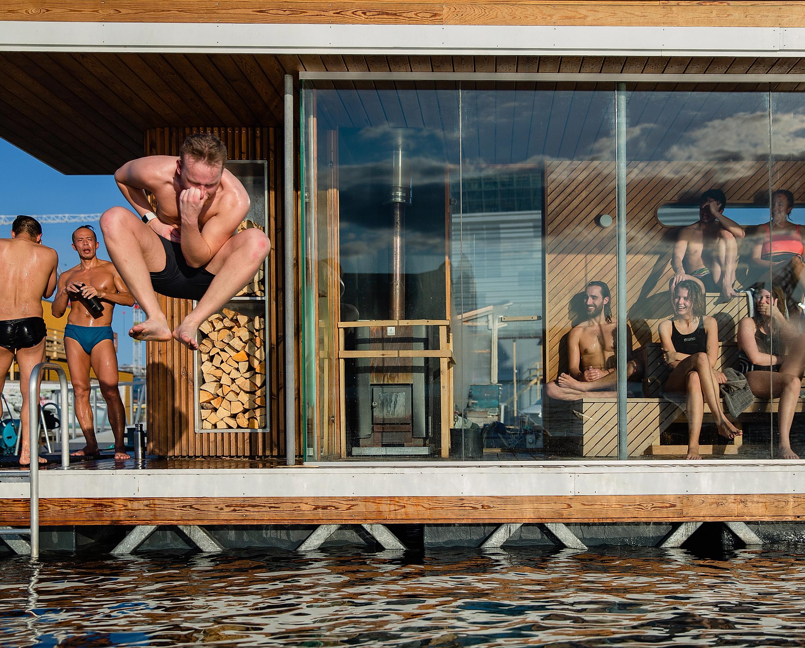 People enjoying a sauna session at Oslo Fjord Sauna. One man is jumping in the sea.