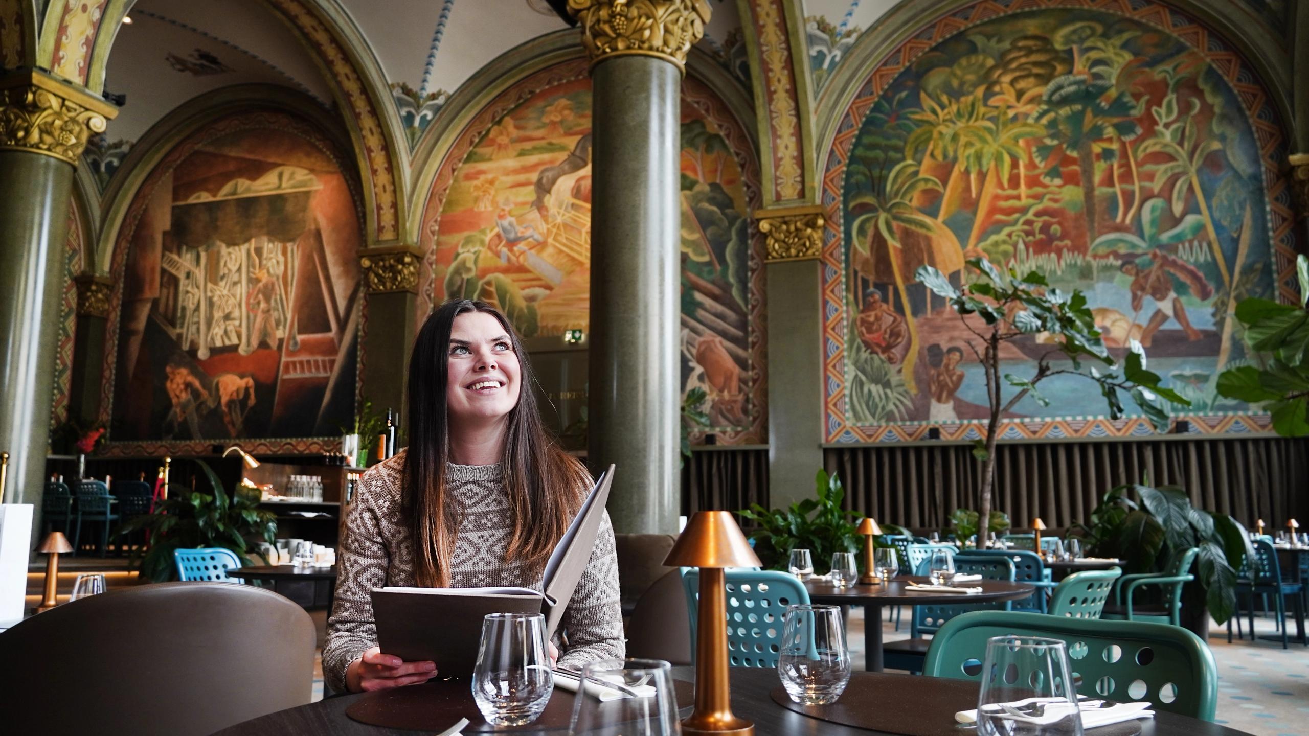 En dame sitter i restauranten Frescohallen - Bergen Børs Hotel