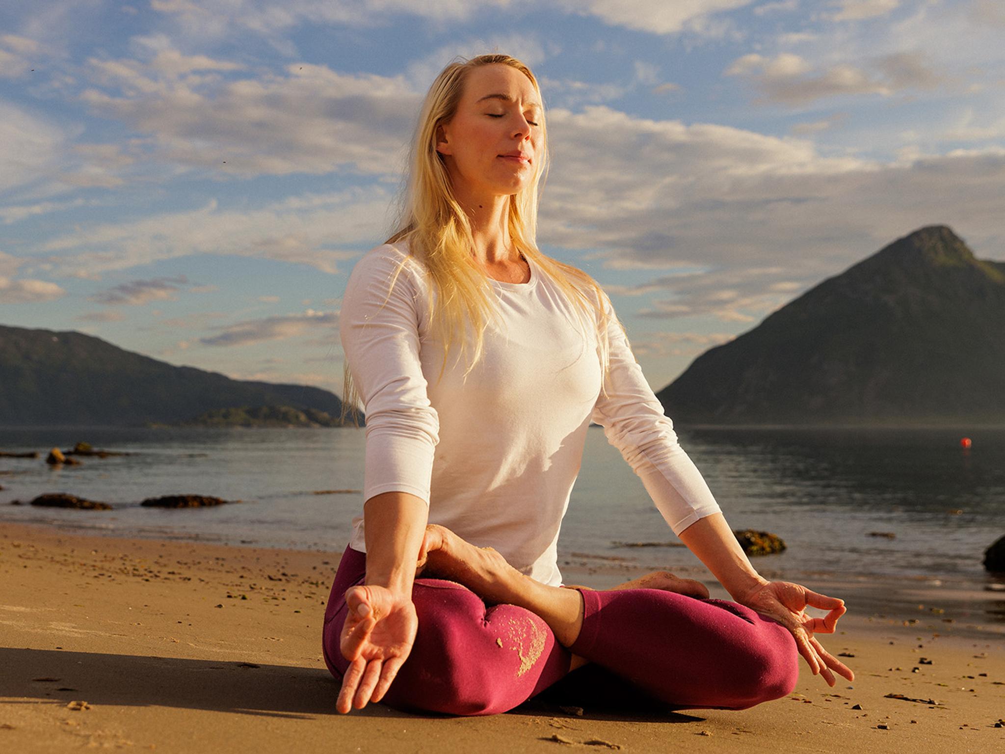 A woman sitting in lotus yoga position on the beach in the midnight sun, Northern Norway.