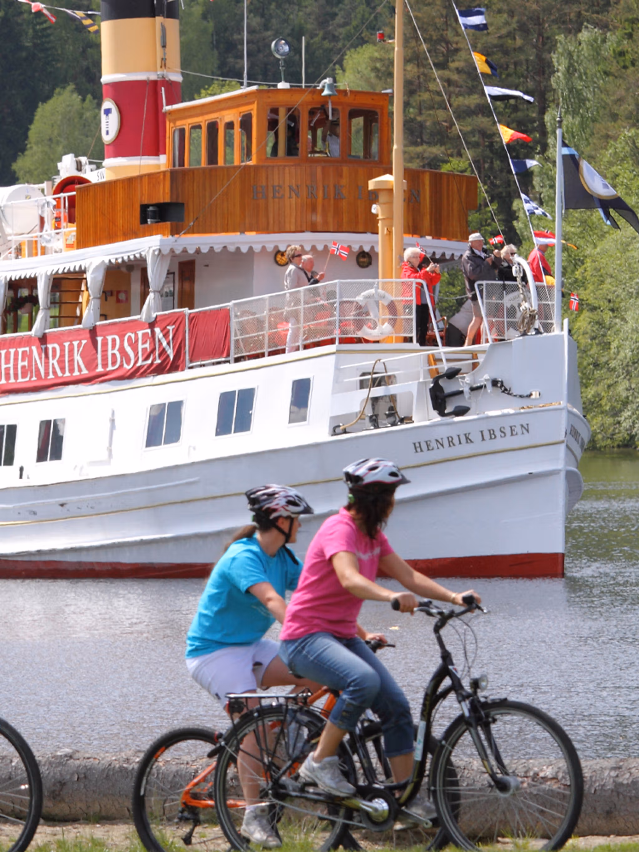 Des cyclistes dépassent un bateau navigant sur le canal, sur la véloroute nationale du canal du Telemark, en Norvège de l’Est