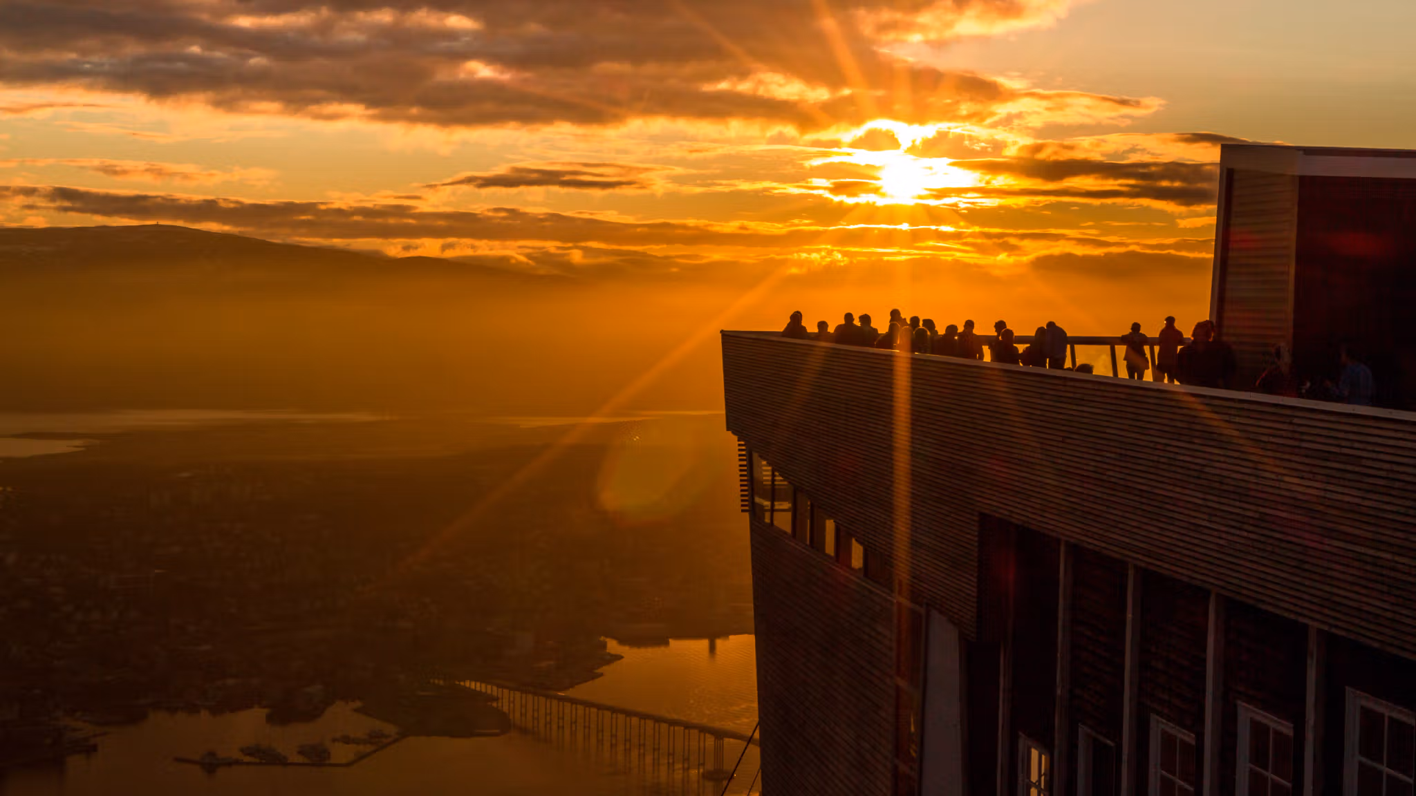 People are standing at the rooftop of the cable car in Tromsø, Northern Norway, admiring the midnight sun.