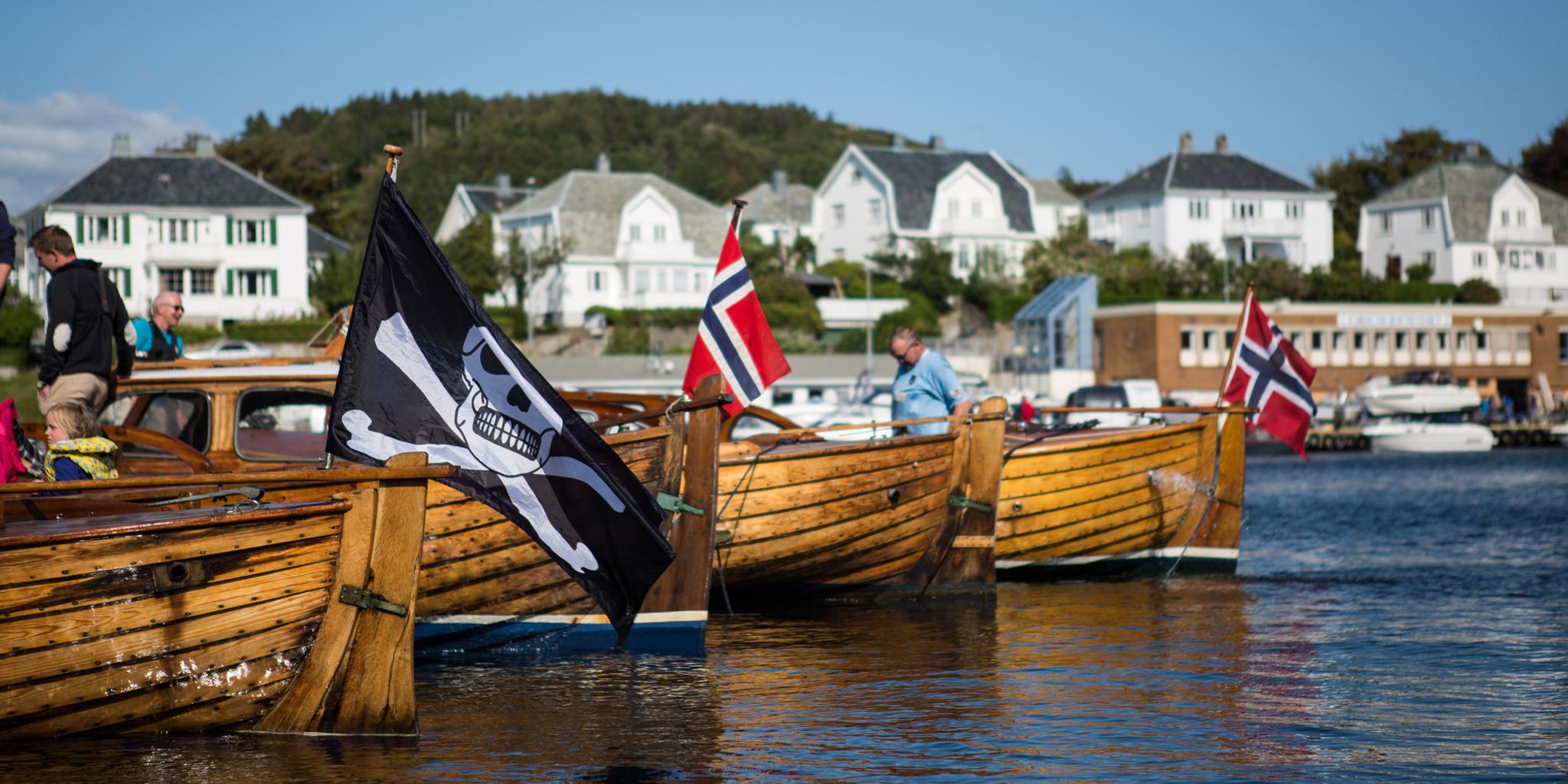 Wooden boats, one with a pirate flag, in Farsund, Southern Norway on a summer day.