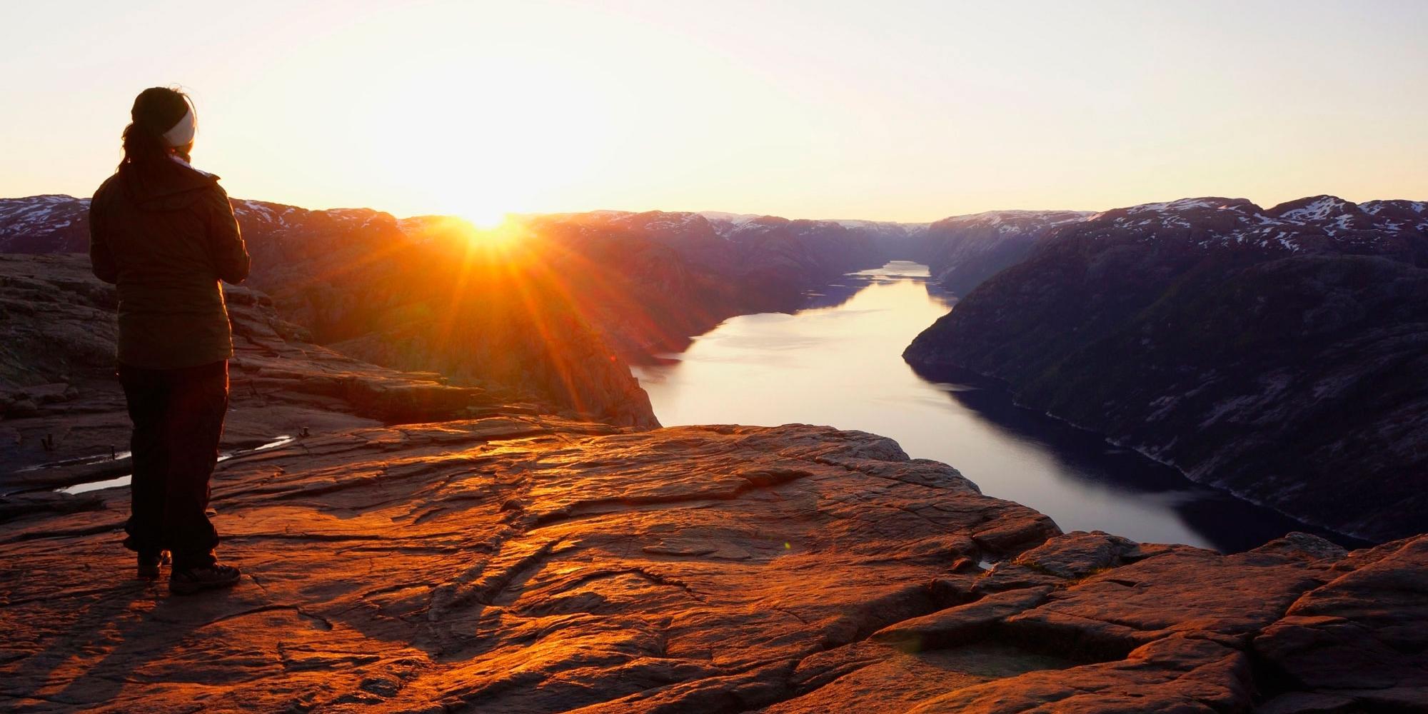 En person ser på soloppgangen fra Preikestolen i Ryfylke i Norge
