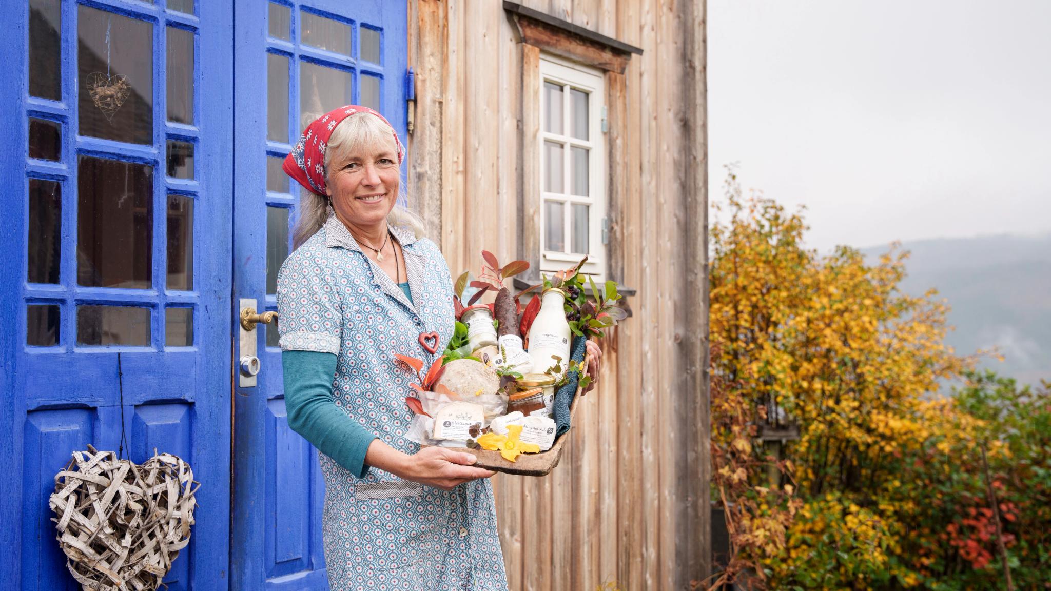 En kvinne holder et trau med lokale produkter utenfor Nørrestogo Gård i Valdres.