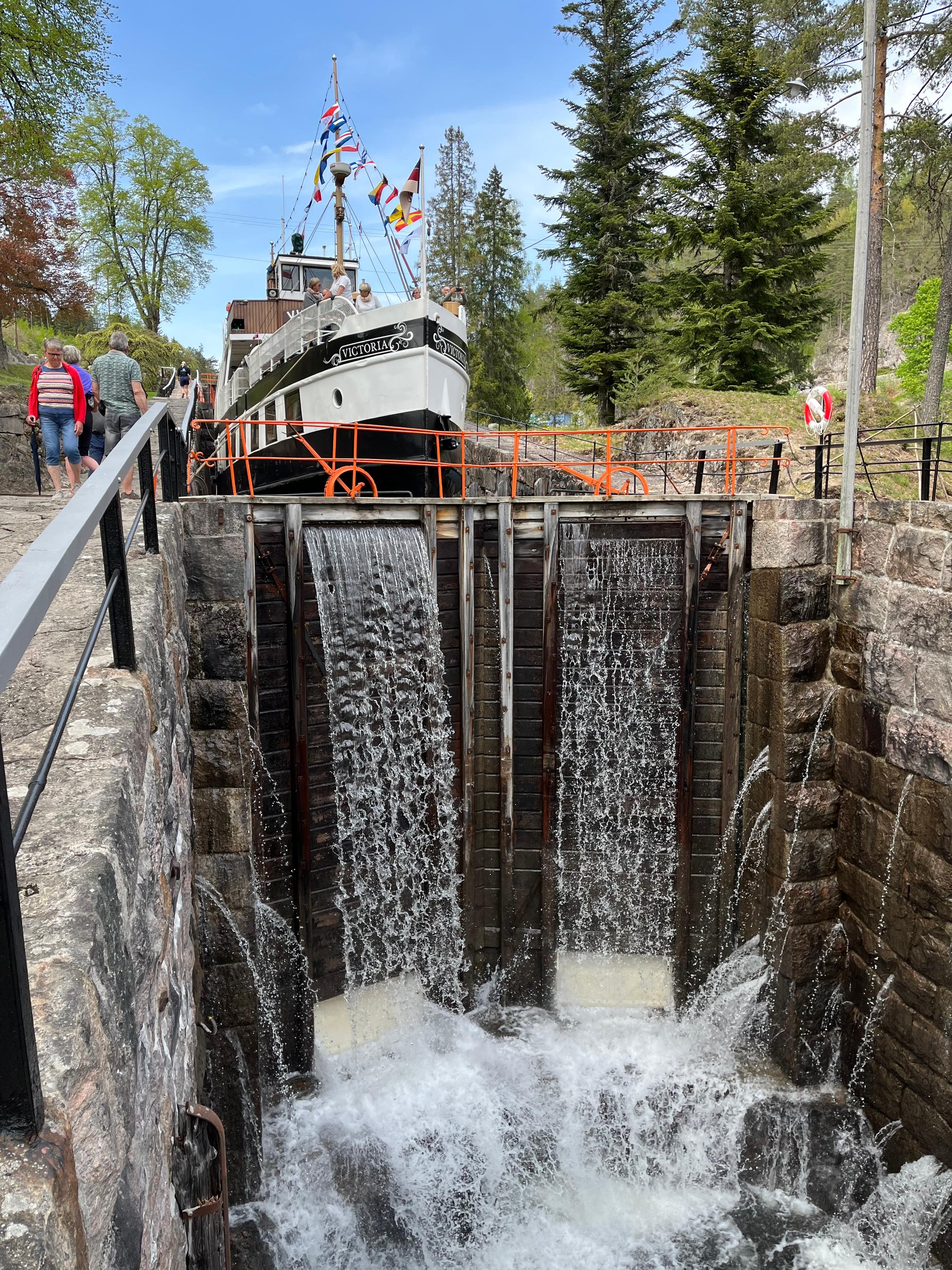 M/S Victoria in a lock chamber at Vrangfoss, with water pouring over the wooden lock gates and passengers on deck.