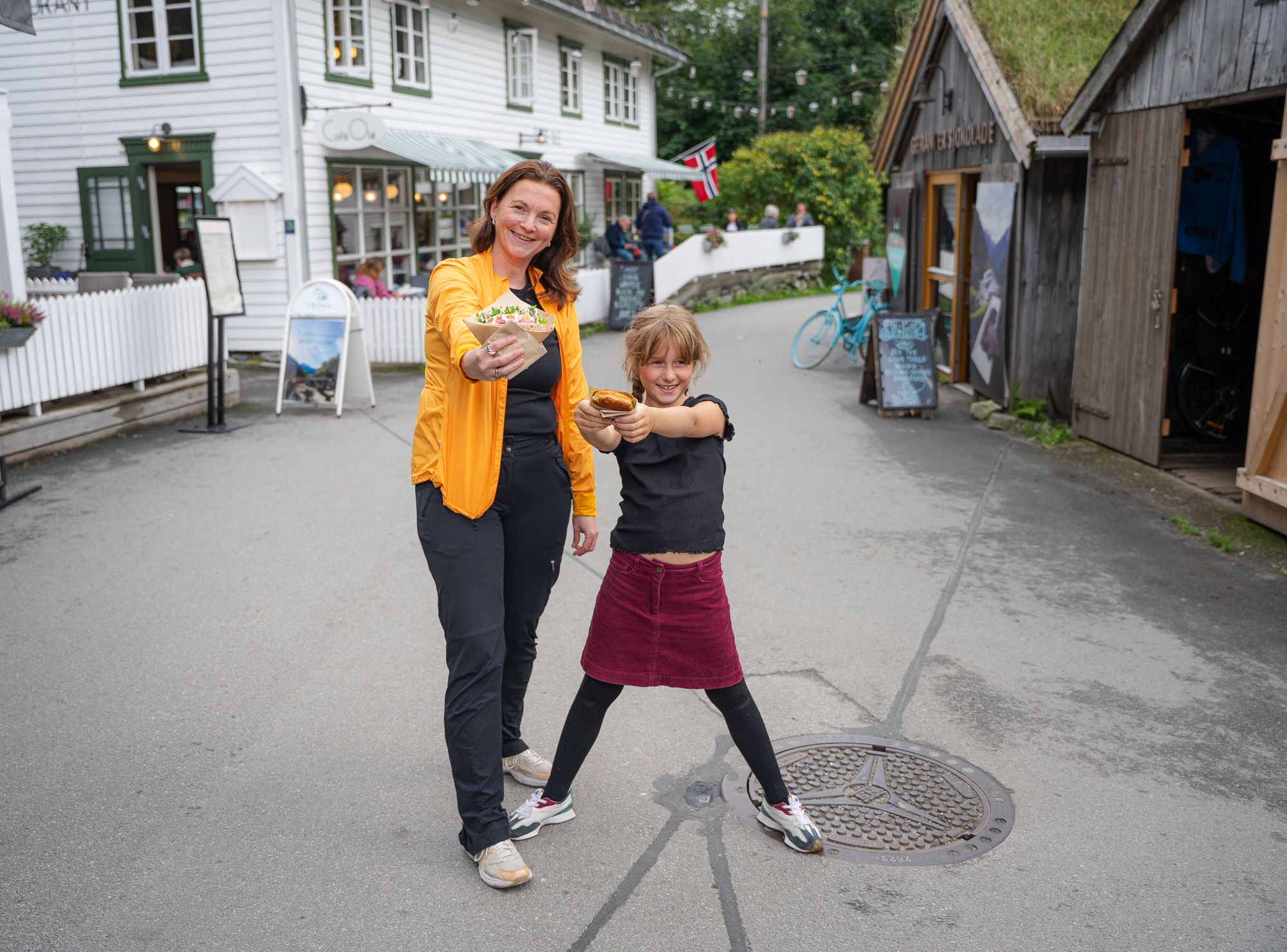 Two people in the middle of a street with food from Fiskekaka in Geiranger.