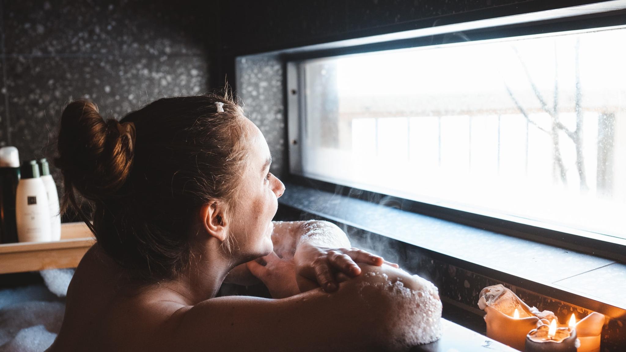 A woman bathing while looking out of the window.