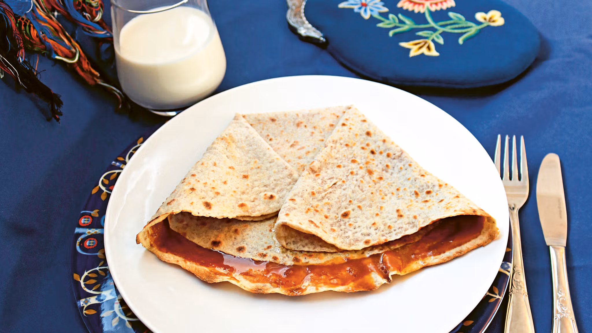 Lefse with a brown cheese spread called "møsbrøm" served on a platter and a glass of milk in Norway