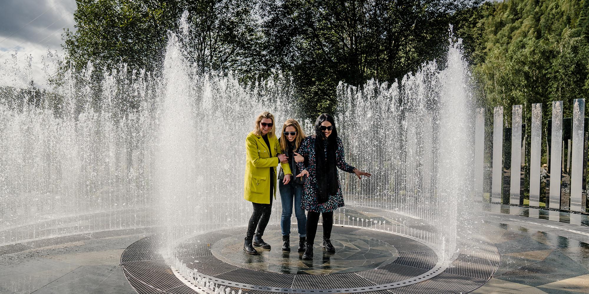 Four laughing women standing in the fountain surrounded by mirrors at Kistefos Museum in Hadeland