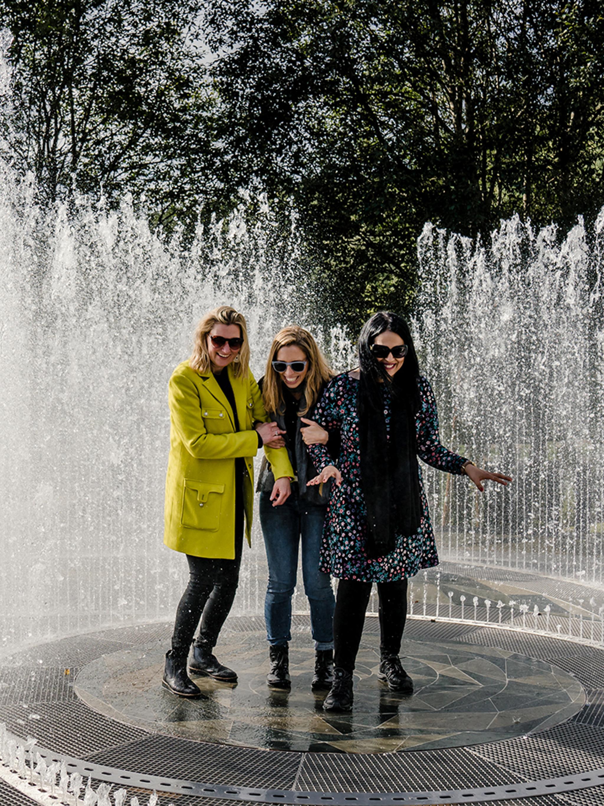 Four laughing women standing in the fountain surrounded by mirrors at Kistefos Museum in Hadeland