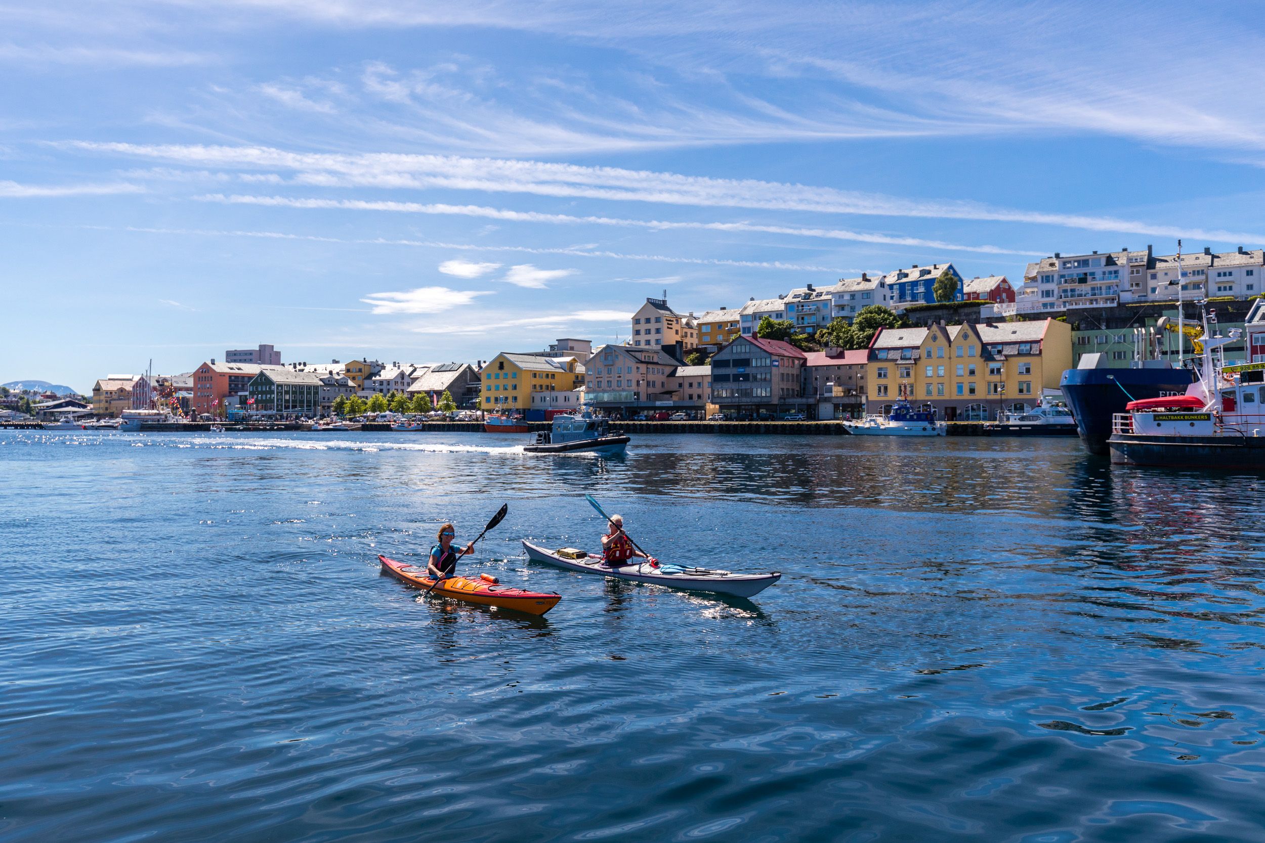 Two people kayaking in the sunlight along the shore of Kristiansund in Fjord Norway.