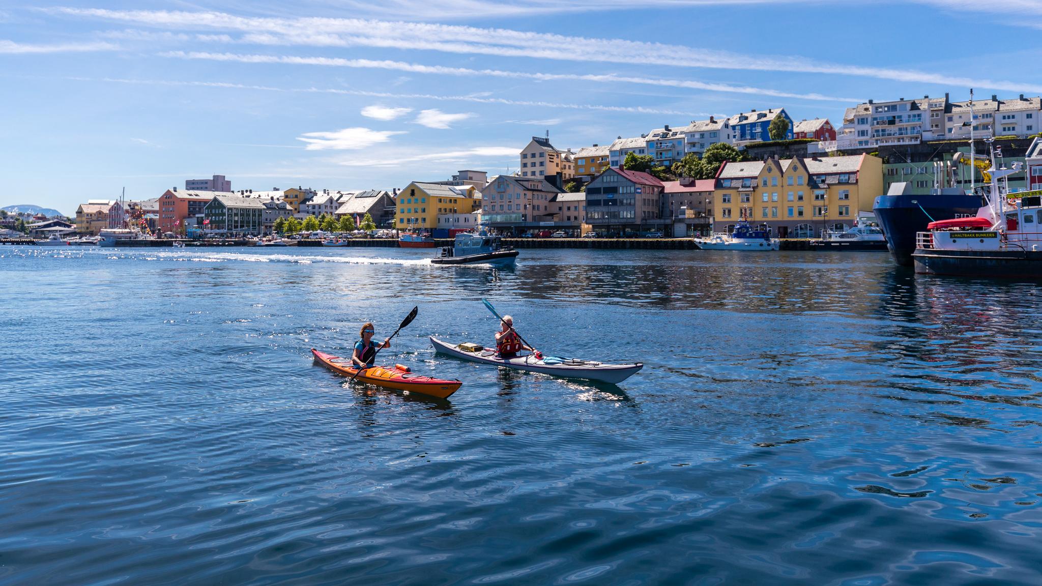 Two people kayaking in the sunlight along the shore of Kristiansund in Fjord Norway.
