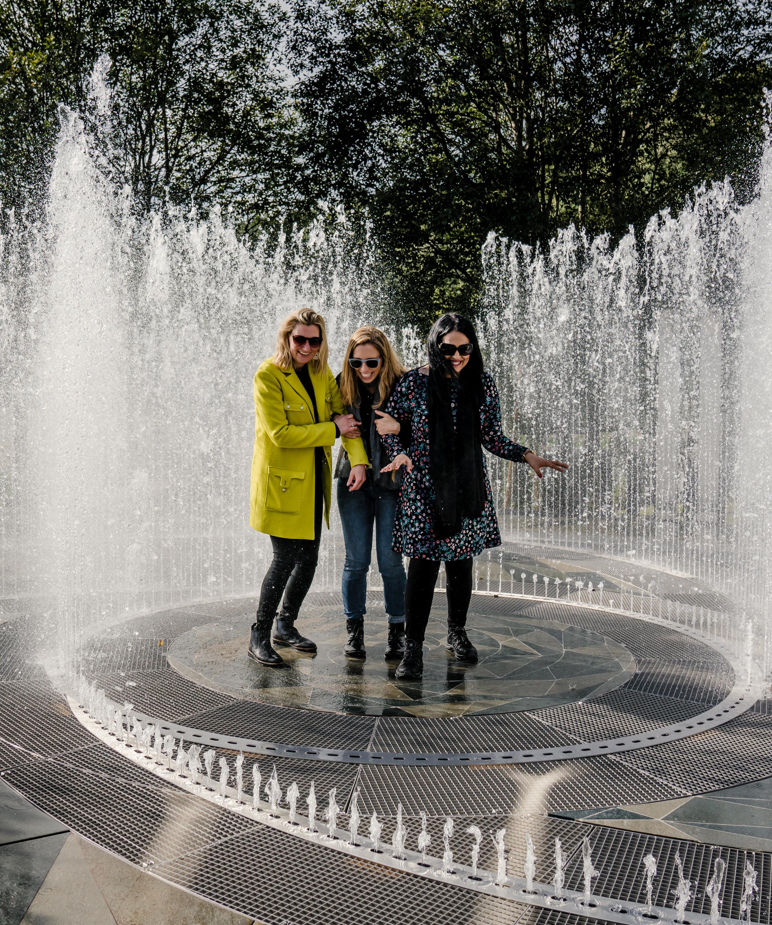 Four laughing women standing in the fountain surrounded by mirrors at Kistefos Museum in Hadeland