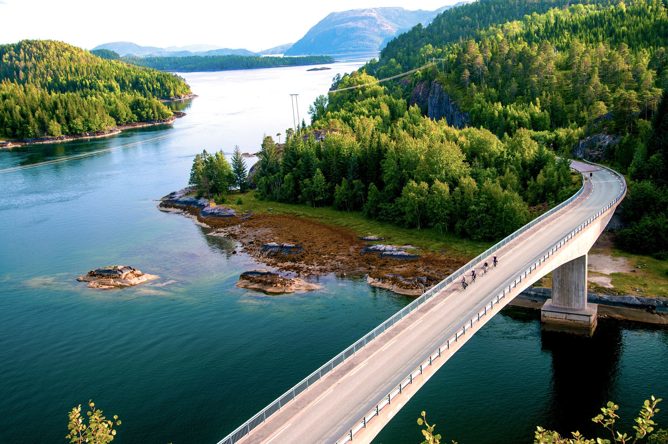 People cycling across a bridge at the Namdalskysten coast in Trøndelag on a sunny summer day